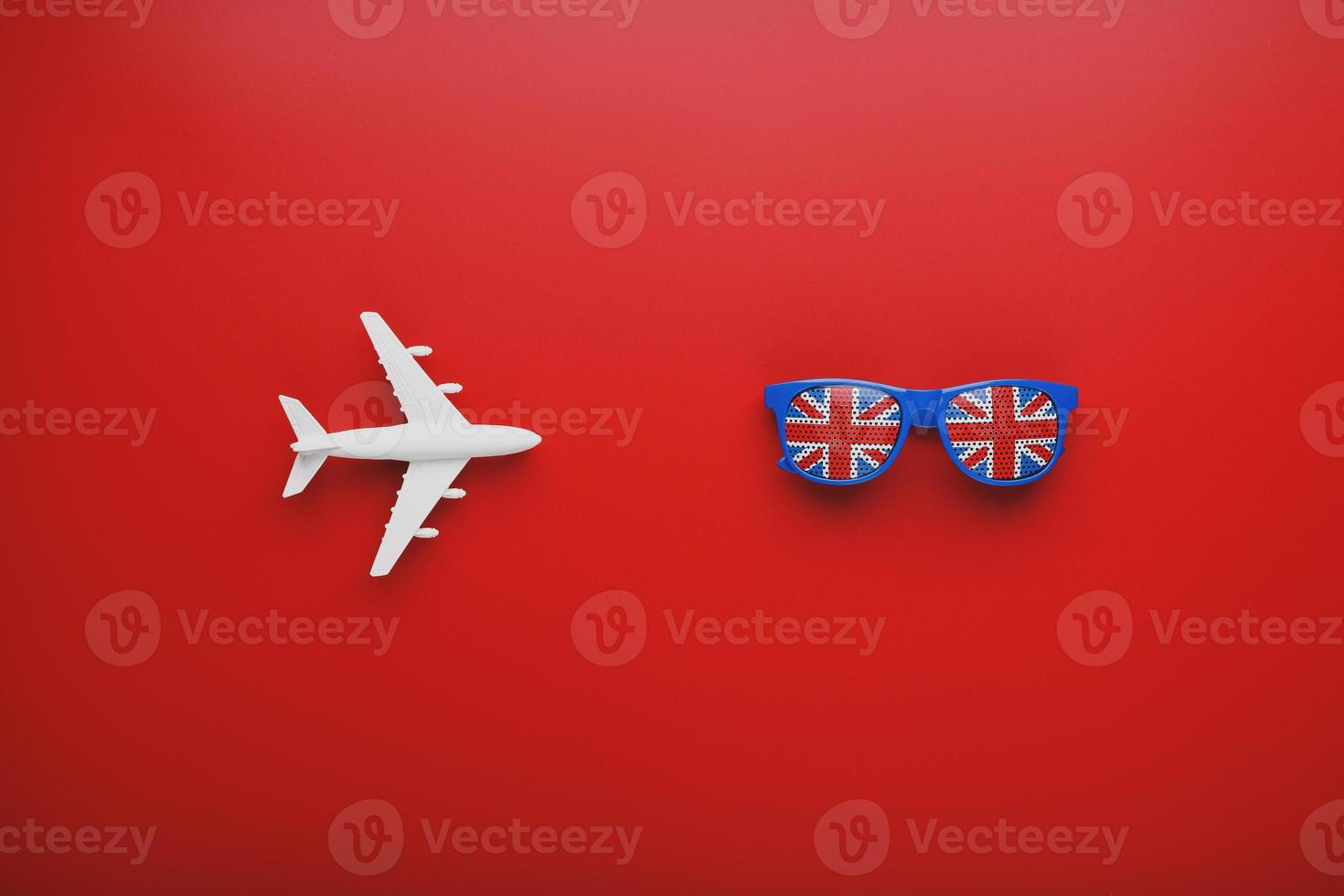 avión blanco y gafas de sol con la bandera del reino unido sobre un fondo rojo. viajar a inglaterra. foto