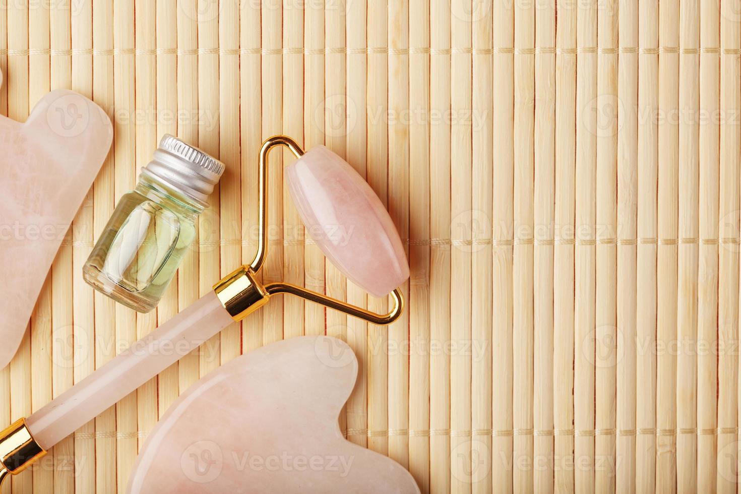 un conjunto de herramientas para la técnica de masaje facial gua sha fabricado en cuarzo rosa natural. rodillo, piedra de jade y aceite en un frasco de vidrio, sobre un fondo de paja para el cuidado de la cara y el cuerpo. foto
