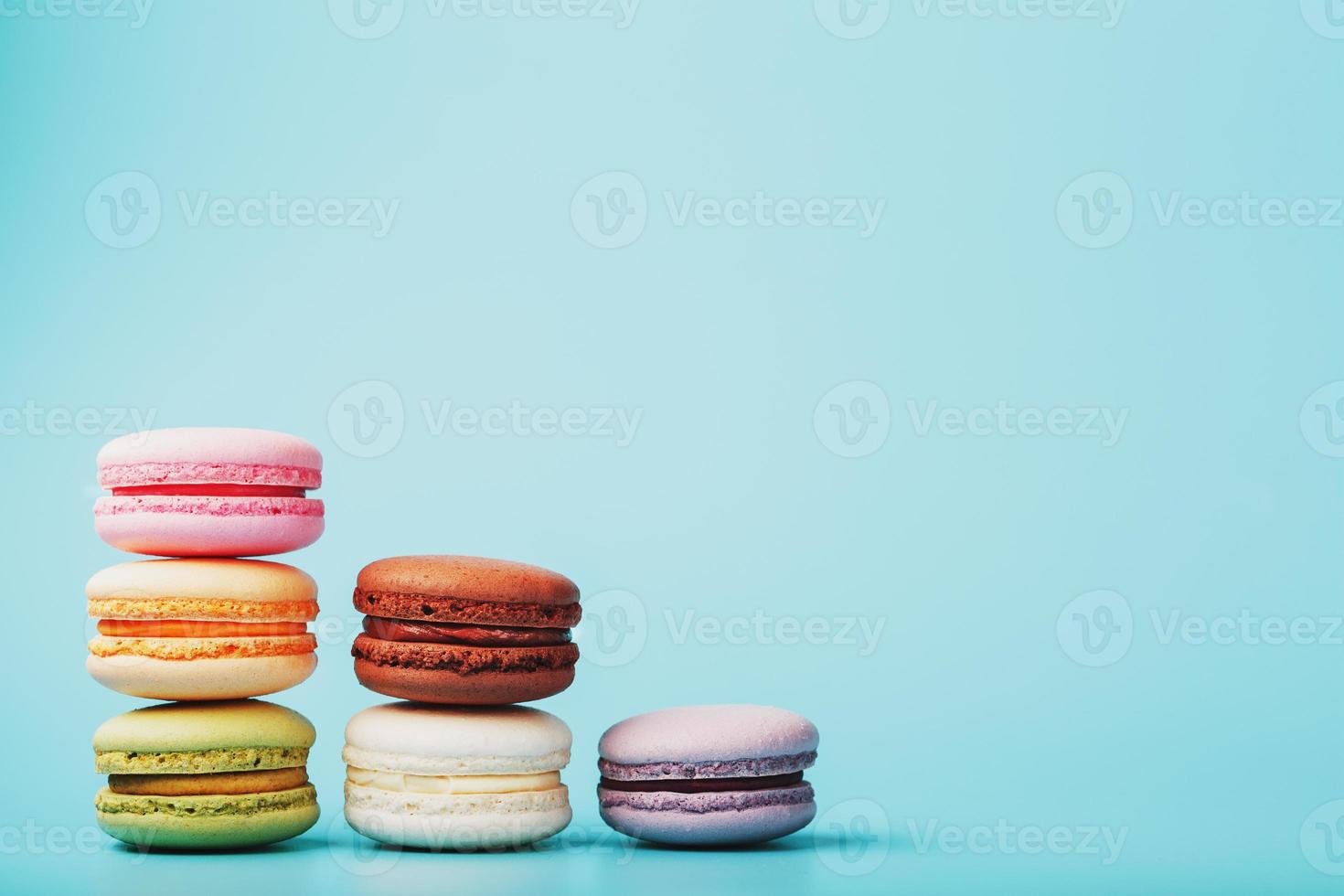 Macaroni cookies of different colors are arranged in the shape of pyramid steps on a blue background. photo