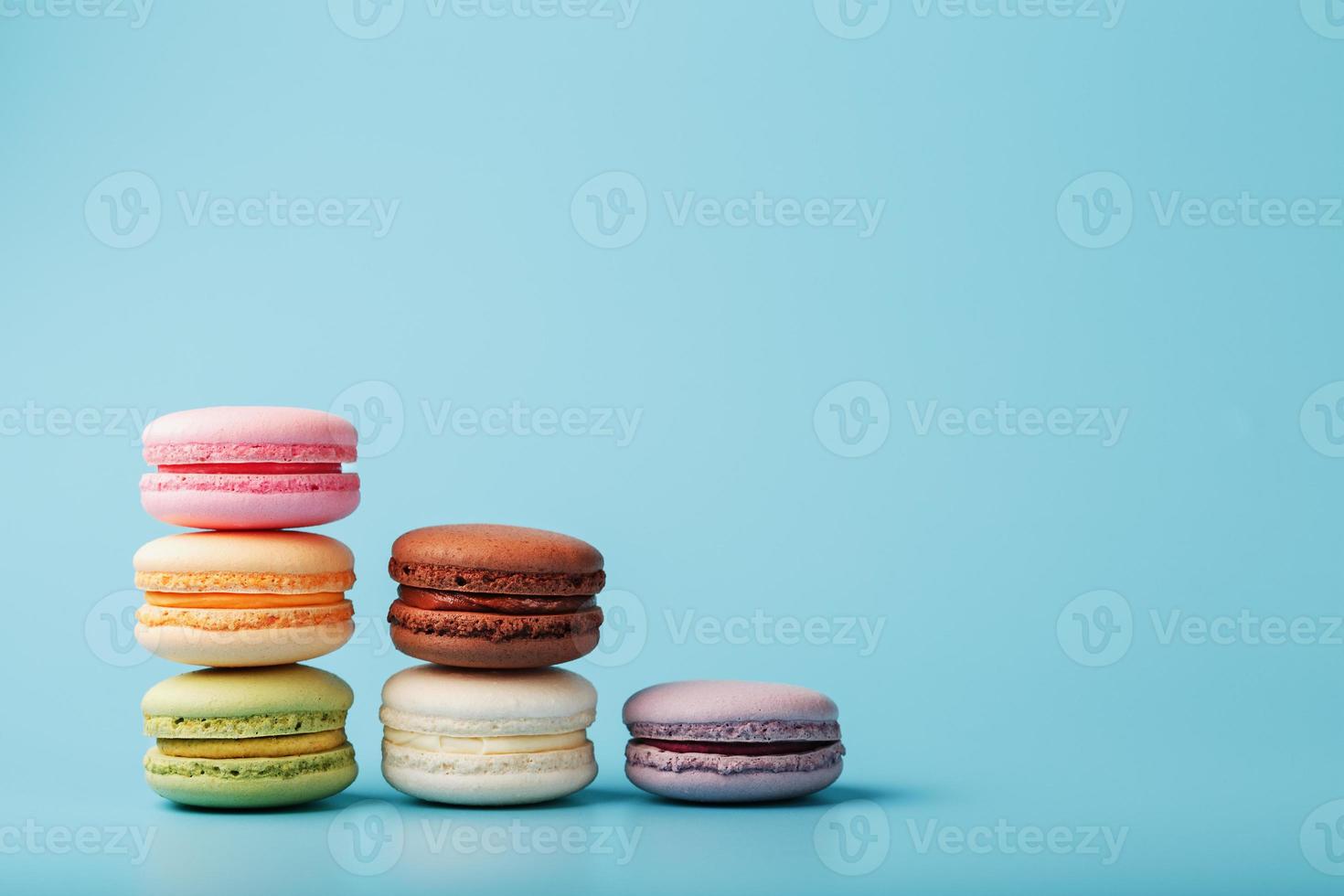 Macaroni cookies of different colors are arranged in the shape of pyramid steps on a blue background. photo