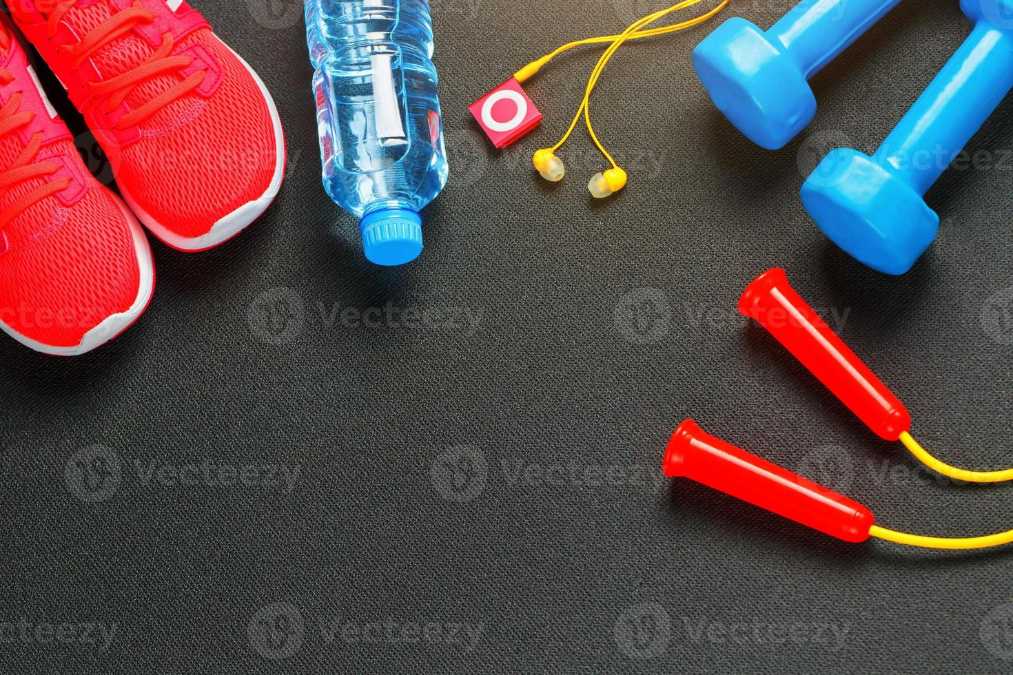 Top view of sports equipment, dumbbells, a skipping rope, a bottle of water, sneakers and a player. Isolated on a gray photo