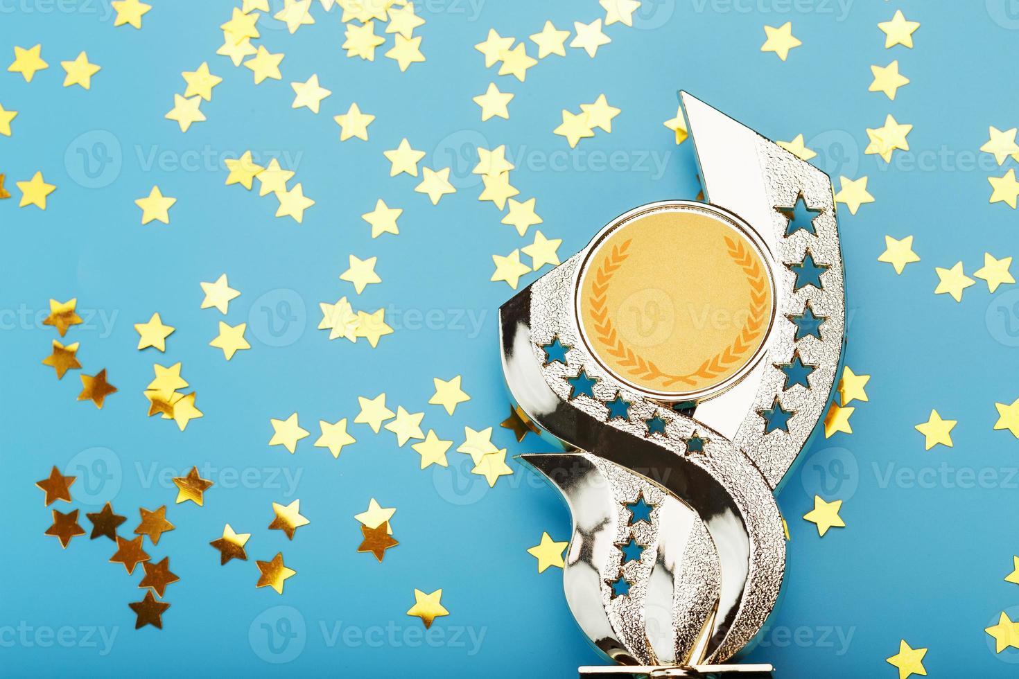 copa de trofeo de oro con estrellas celebrando el éxito en un fondo azul. foto
