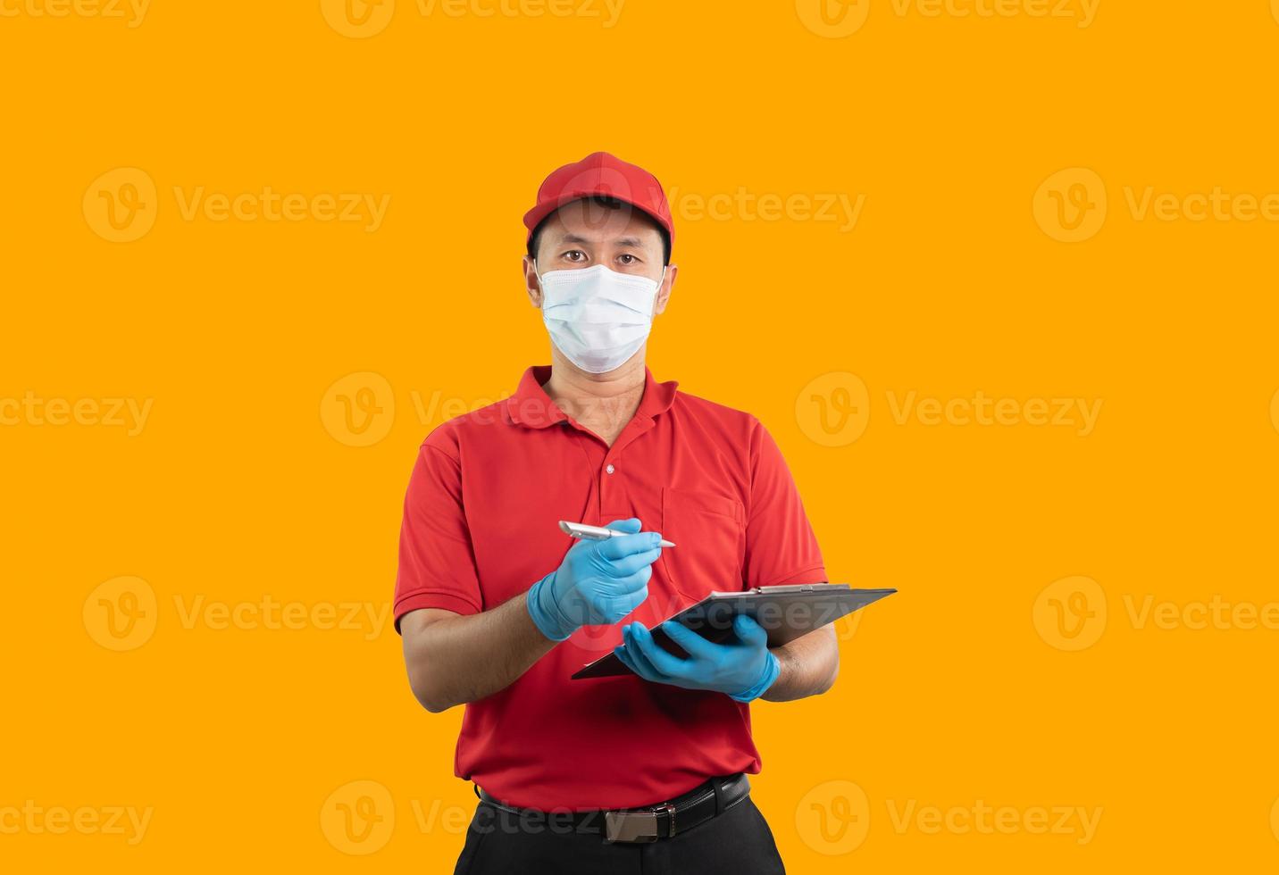 Asian delivery man worker smiling in red uniform working on document isolated on orange background, checking list parcel boxes for sending or conveying parcels by mail. Logistic transport post office. photo