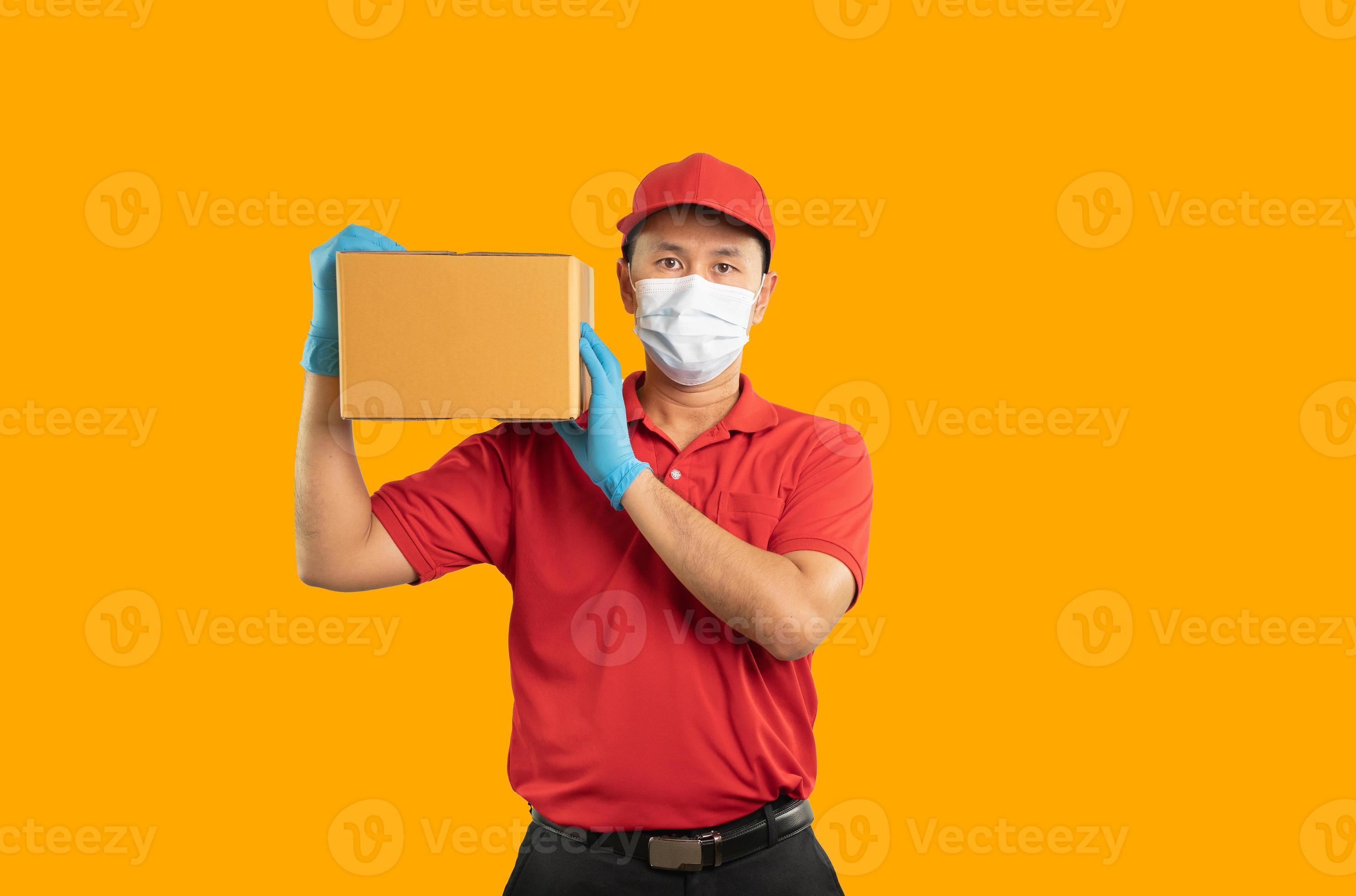 Delivery man in gloves and mask holds box on yellow background