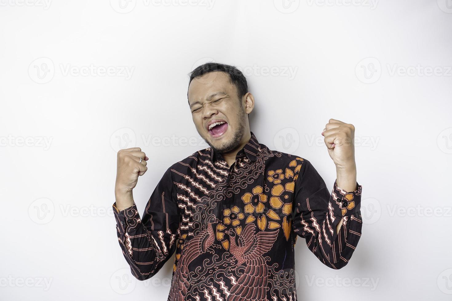 A young Asian man with a happy successful expression wearing batik shirt isolated by white background photo