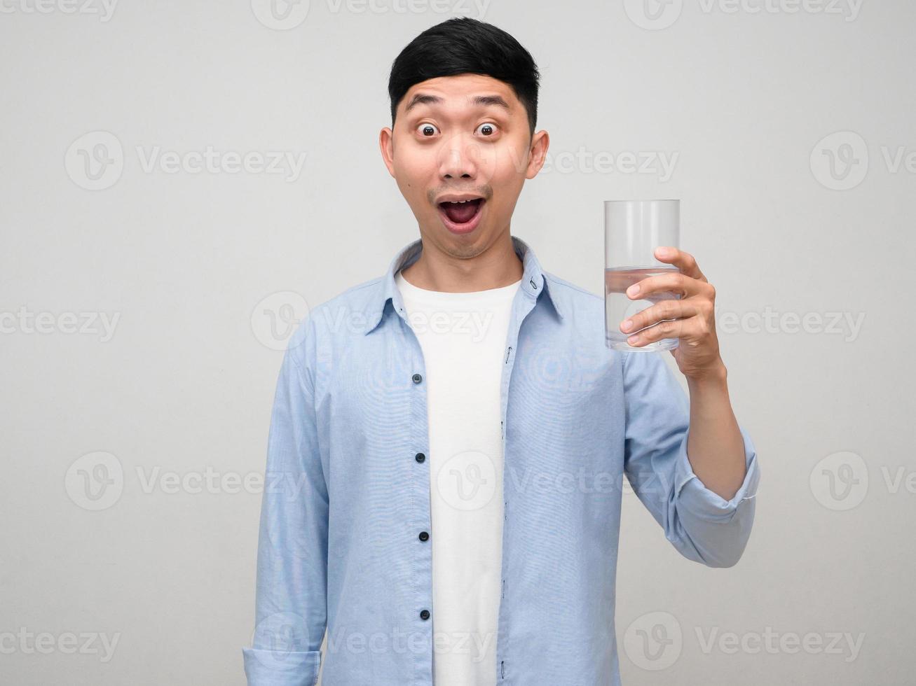 Young positive man blue shirt hold glass of water feels amazed isolated photo