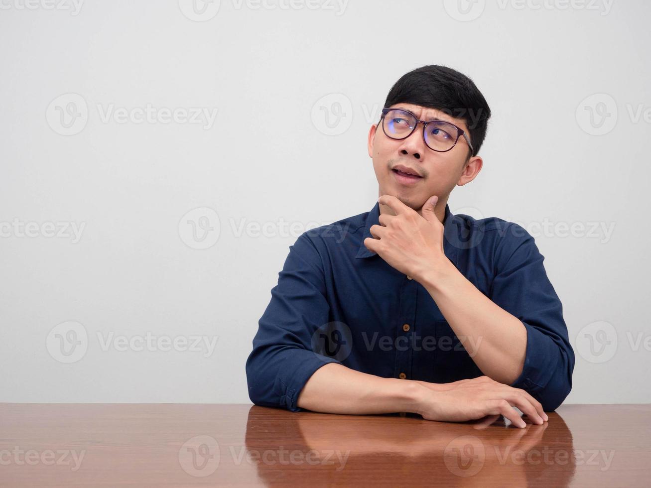 Asian businessman wear glasses sit at the table thoughtful gesture looking at copy space photo