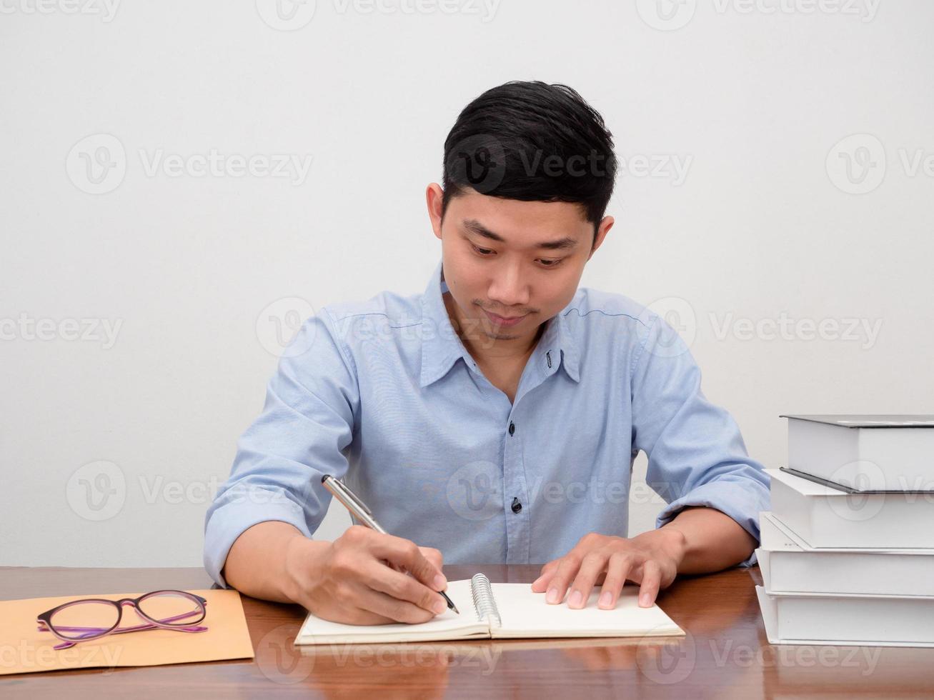 Positive asian businessman sit at workplace table writing on the book photo