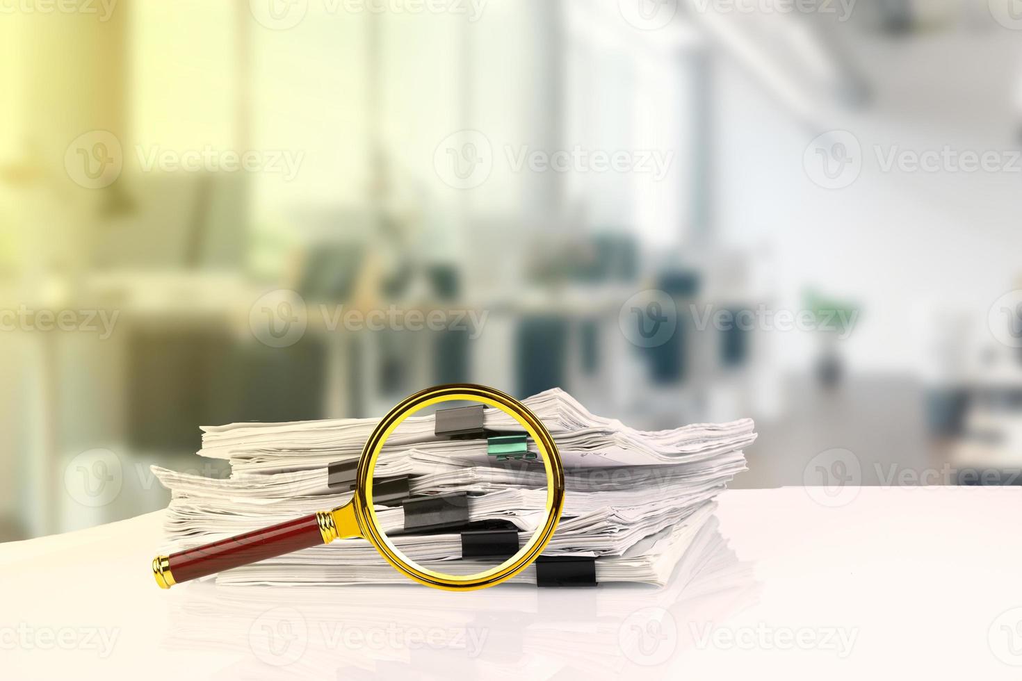 A business office, a stack of office papers and a magnifying glass on the desk. photo