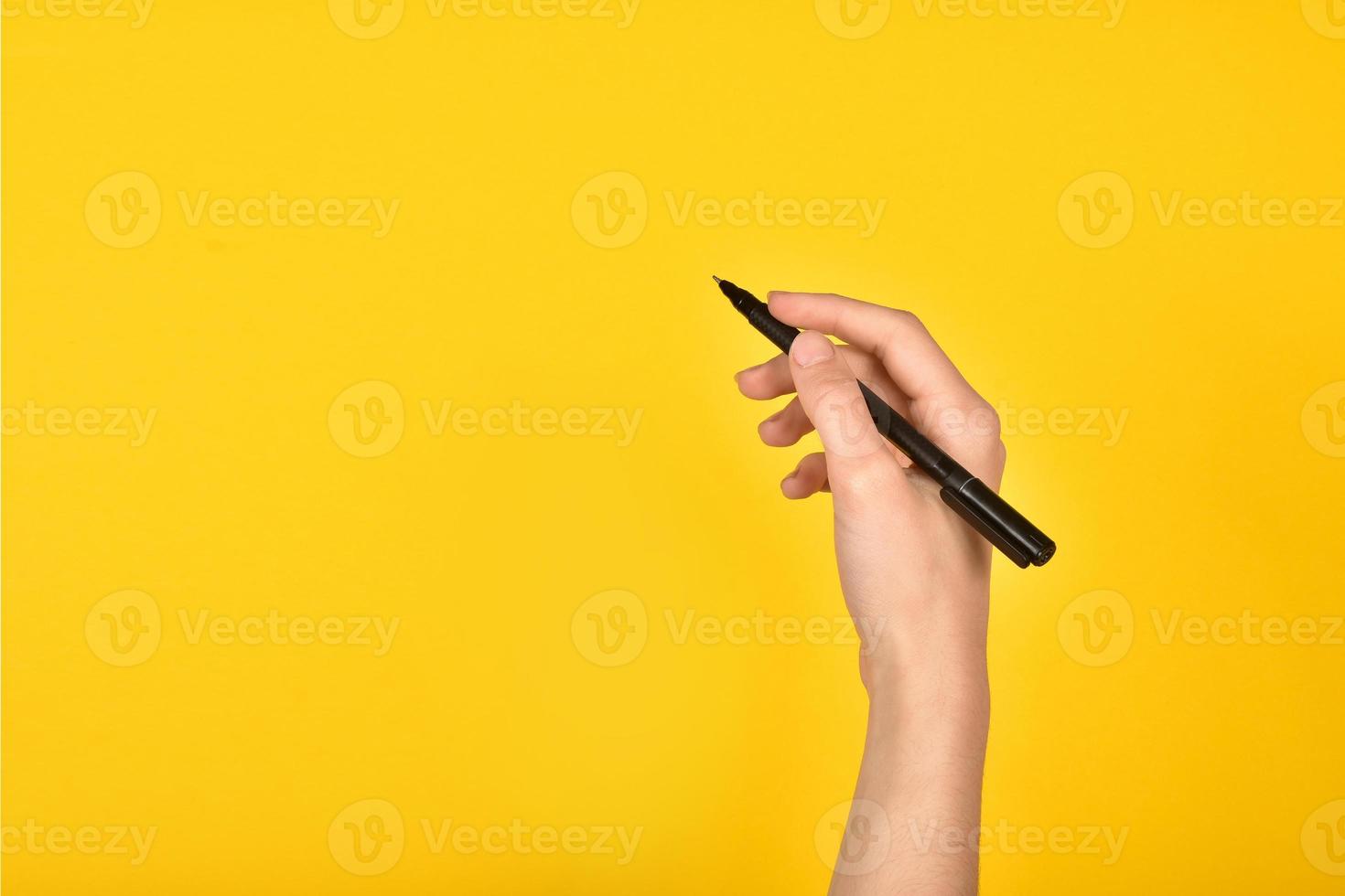 Girl's hand with a pen on a yellow background. Advertising inscription. photo