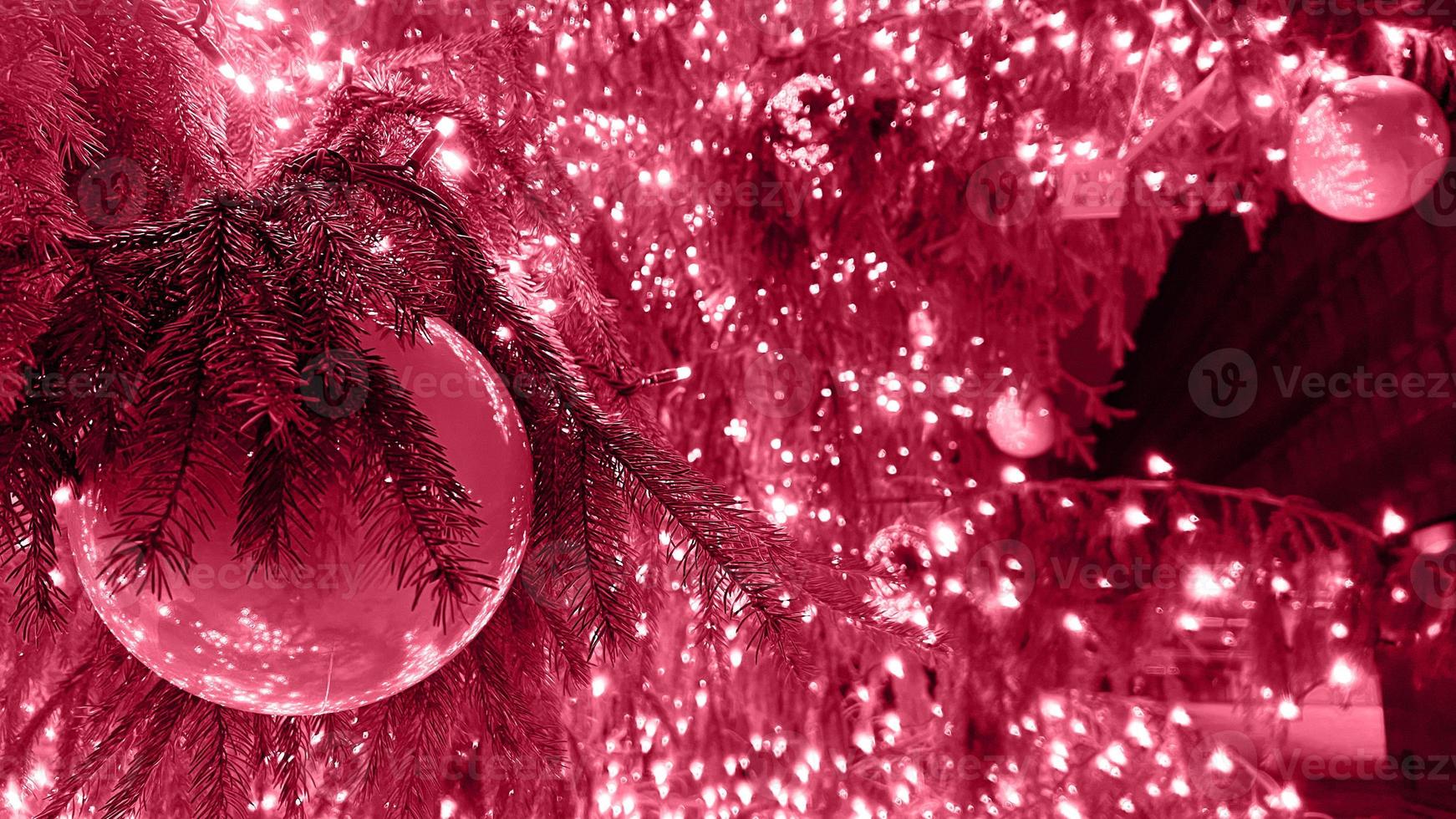 Closeup branches of coniferous tree decorated with glittering balls and shiny light garland on Christmas day at home. Color Of The Year 2023 - Viva Magenta photo
