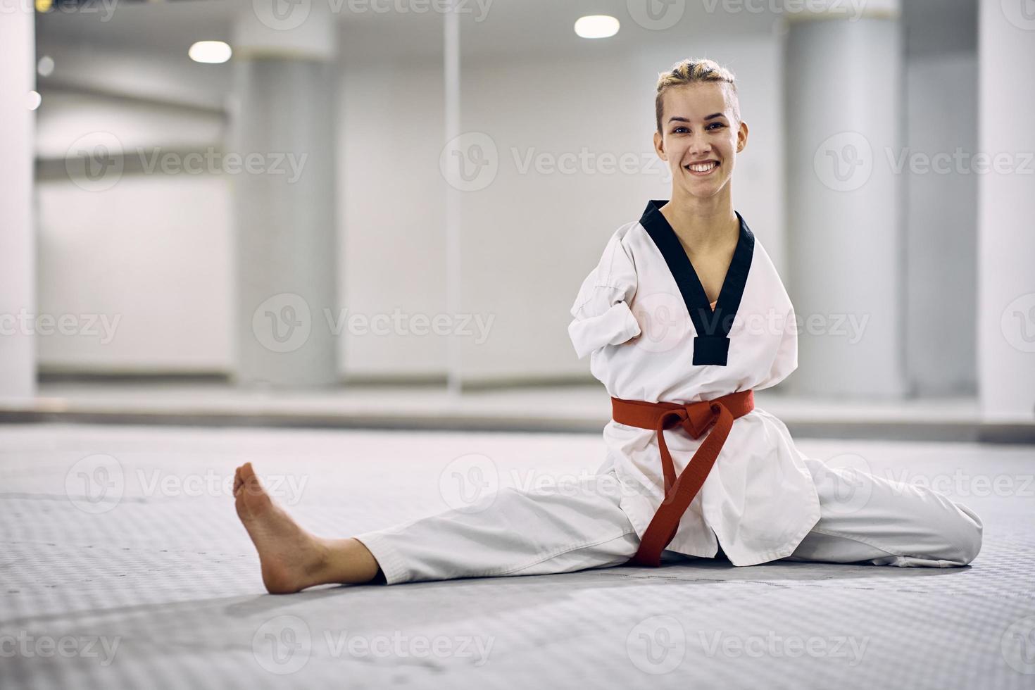 feliz atleta femenina de artes marciales con discapacidad calentándose mientras ejercita taekwondo en el club de salud. foto