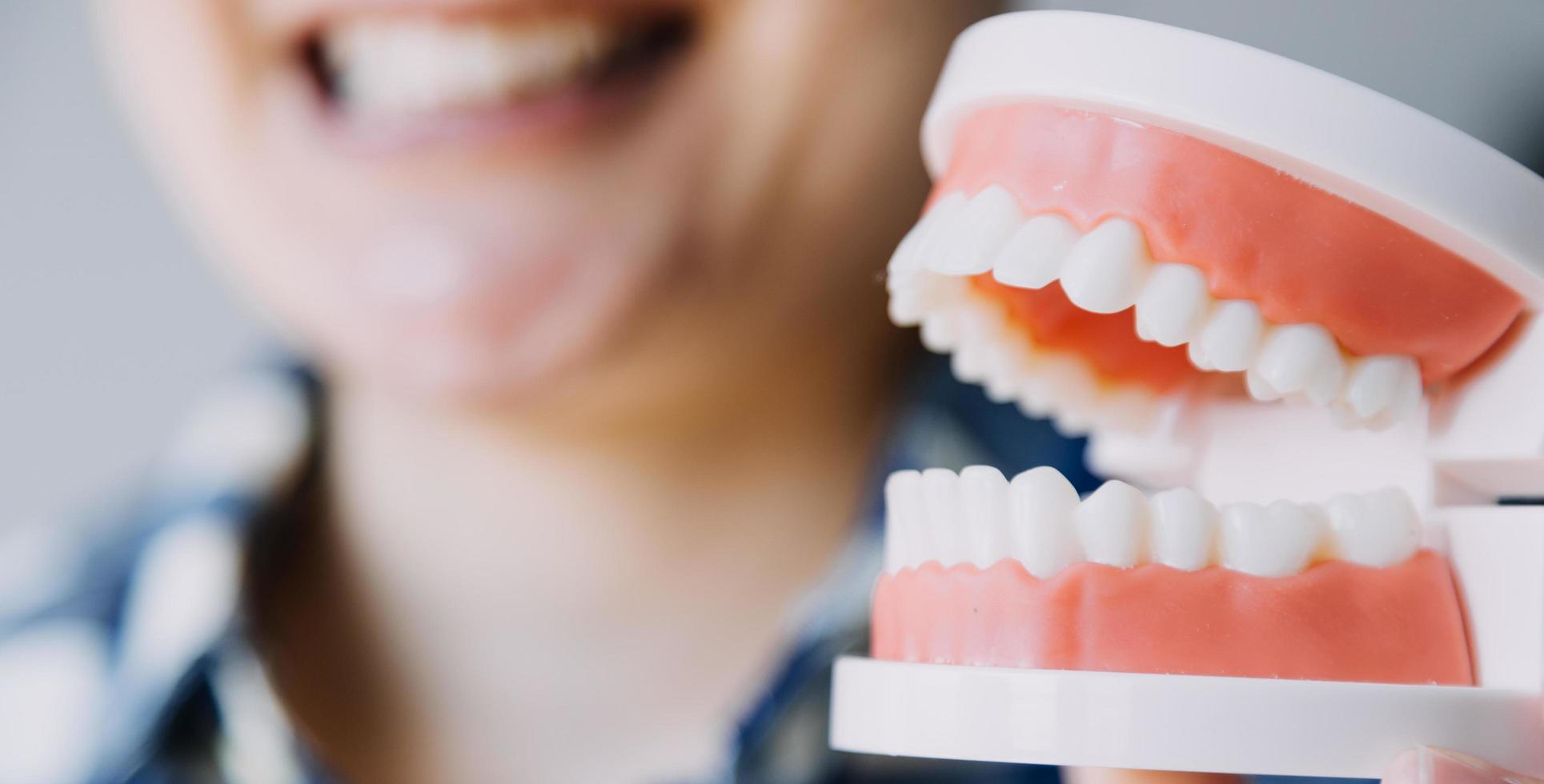 concepto de estomatología, retrato parcial de una chica con fuertes dientes blancos mirando la cámara y sonriendo, con los dedos cerca de la cara. primer plano, de, mujer joven, en, dentista, estudio, adentro foto