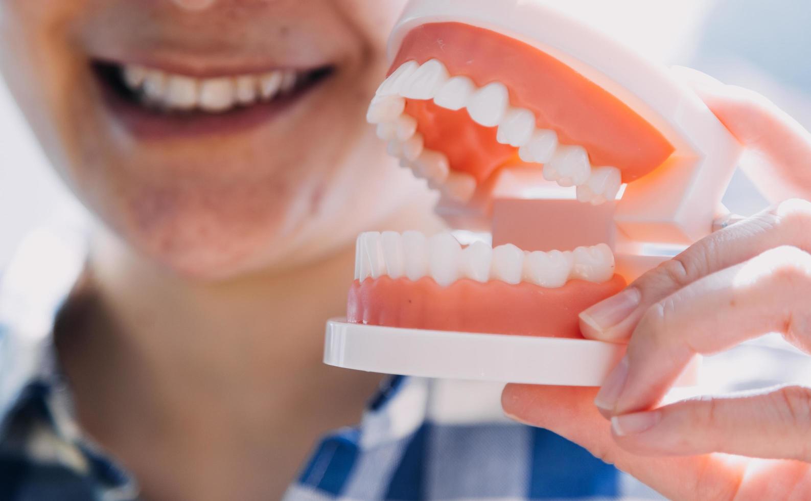 concepto de estomatología, retrato parcial de una chica con fuertes dientes blancos mirando la cámara y sonriendo, con los dedos cerca de la cara. primer plano, de, mujer joven, en, dentista, estudio, adentro foto