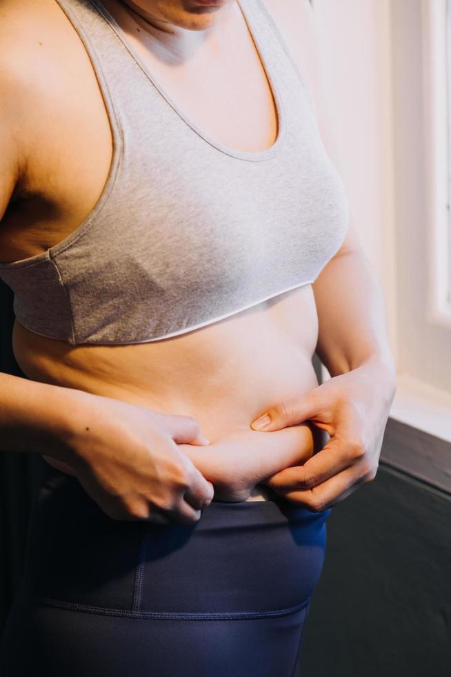 hermosa mujer gorda con cinta métrica usa su mano para exprimir el exceso de grasa que está aislado en un fondo blanco. ella quiere perder peso, el concepto de cirugía y descomponer grasa bajo el foto