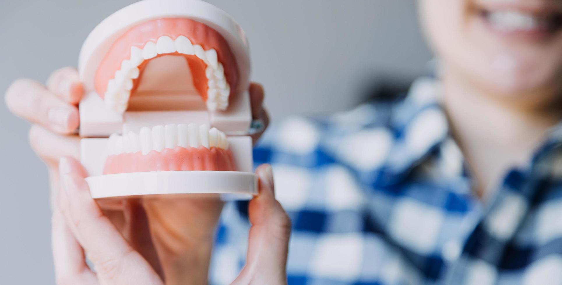 concepto de estomatología, retrato parcial de una chica con fuertes dientes blancos mirando la cámara y sonriendo, con los dedos cerca de la cara. primer plano, de, mujer joven, en, dentista, estudio, adentro foto