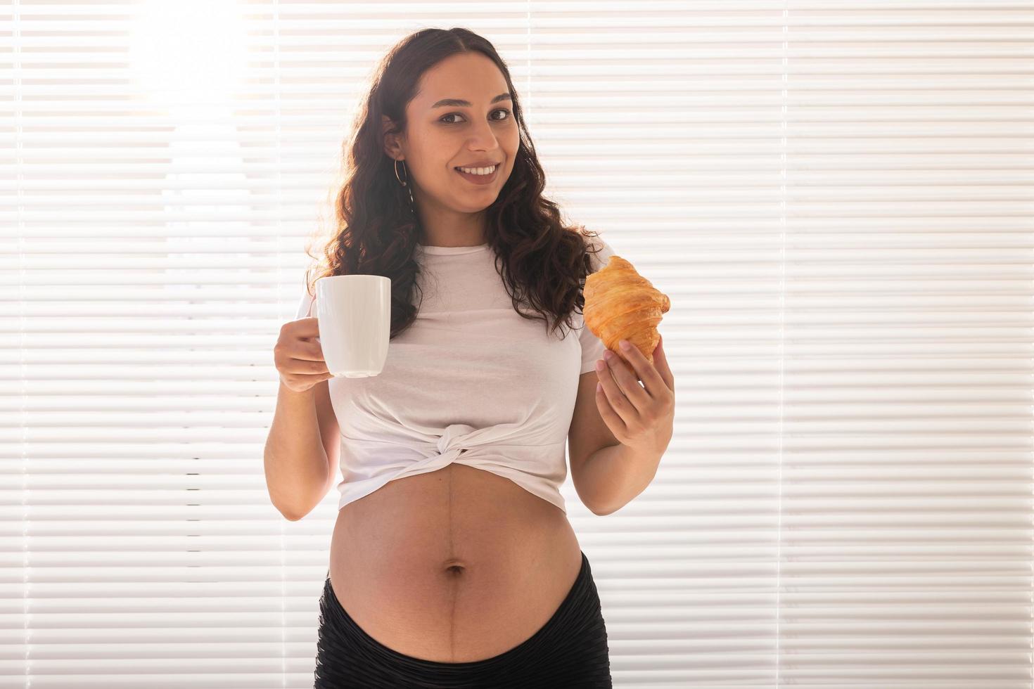 Happy pregnant woman with croissant buns at home. Pregnancy, eating and people concept. Copyspace. photo