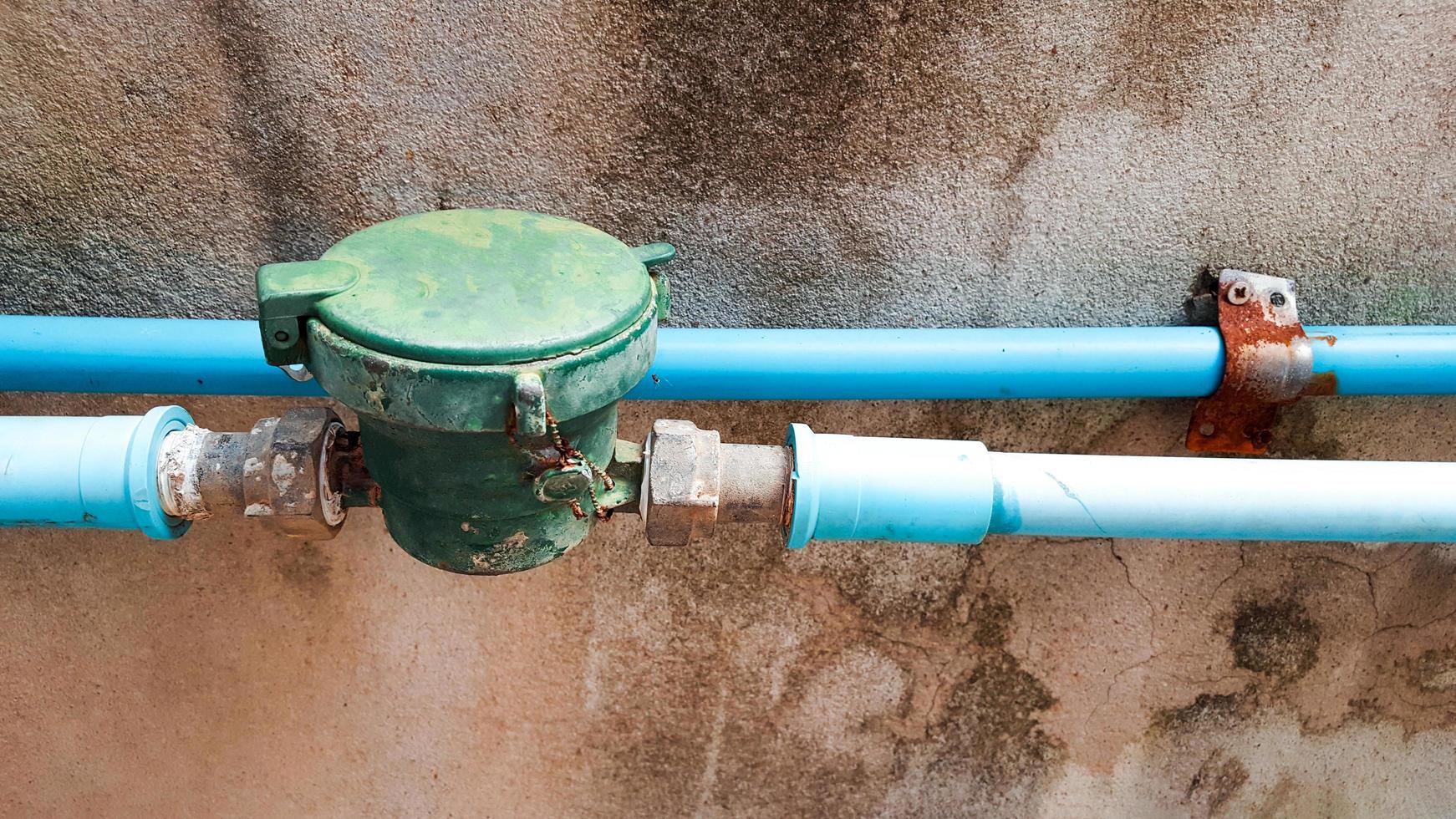 Old green water meter connected to the blue water pipes photo