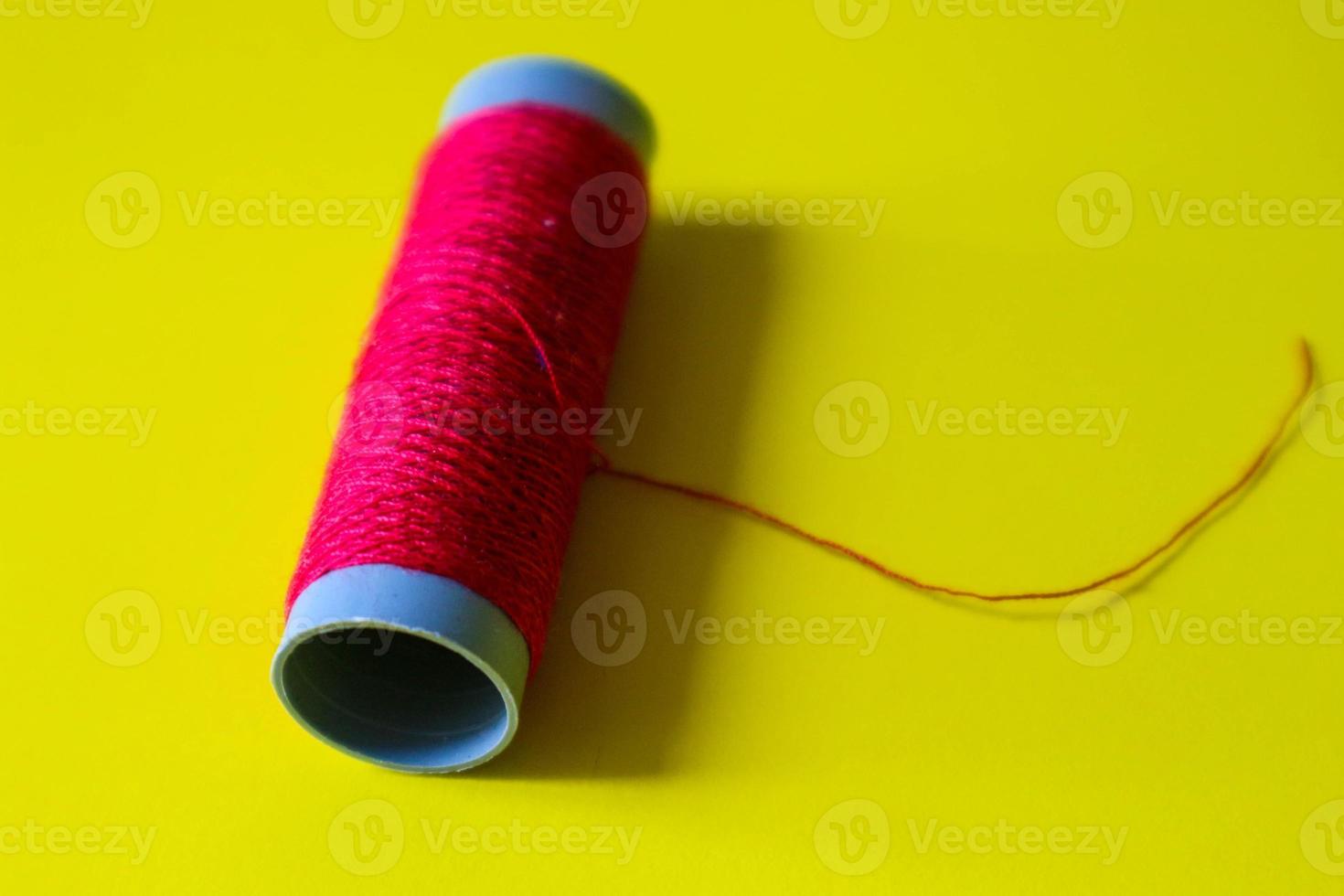 Isolated photo of a roll of red thread above and in front of a yellow background.