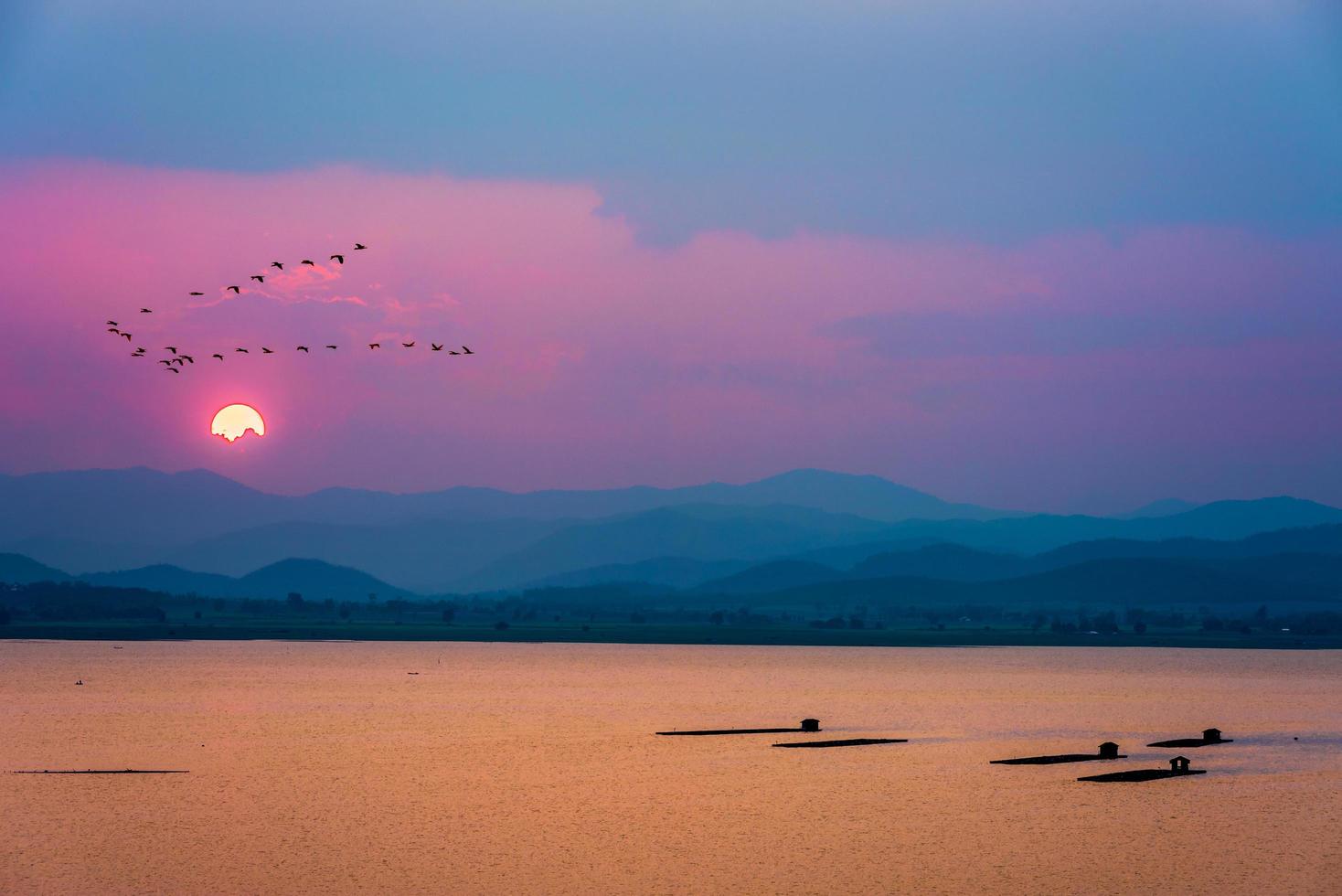 Birds flying over mountains and lake during sunset photo
