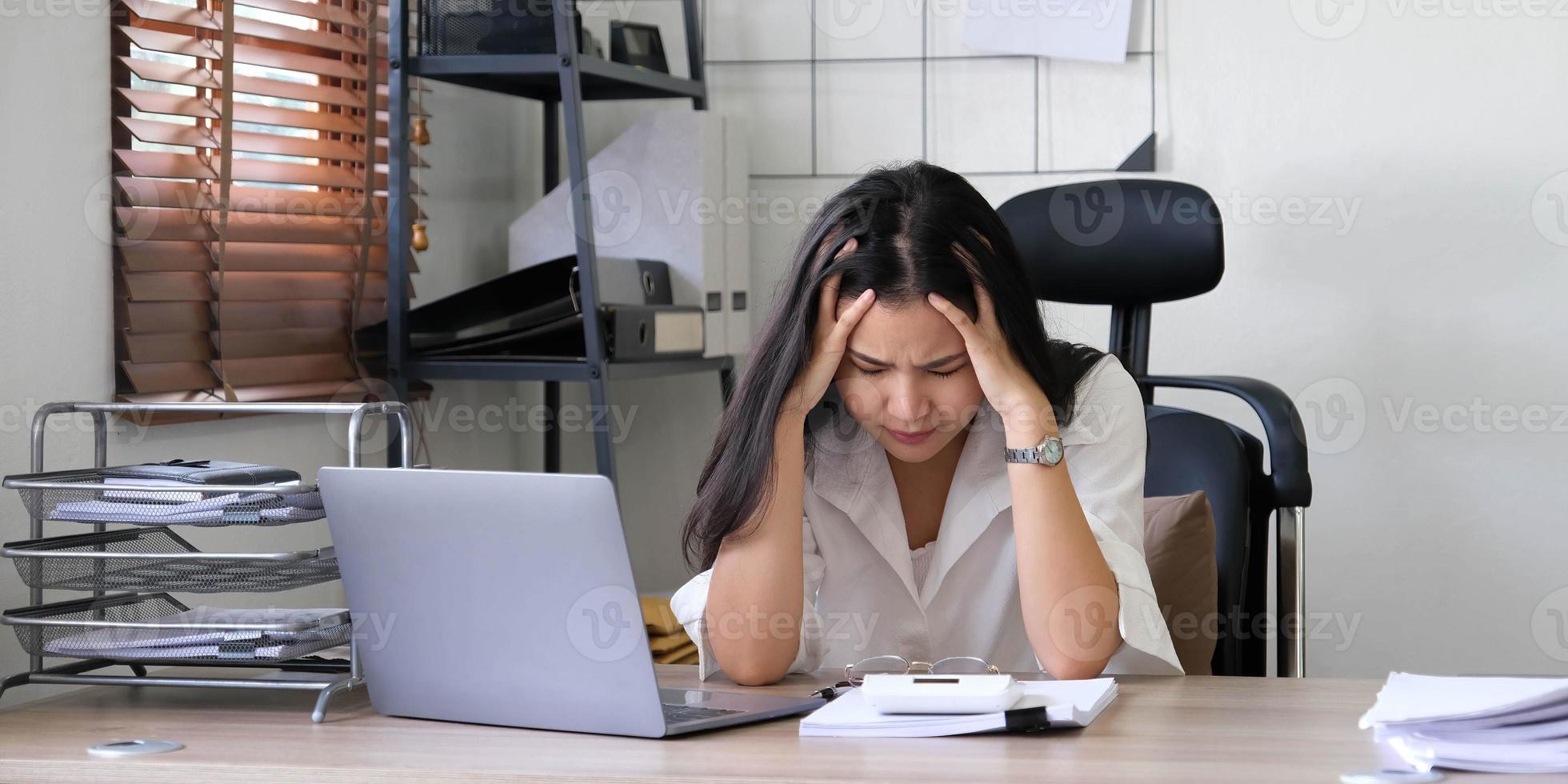 Tired female employee holding head on hand, looking at computer screen, doing hard task, having problem with computer software. Stressed exhausted businesswoman suffering from headache, feeling bored. photo