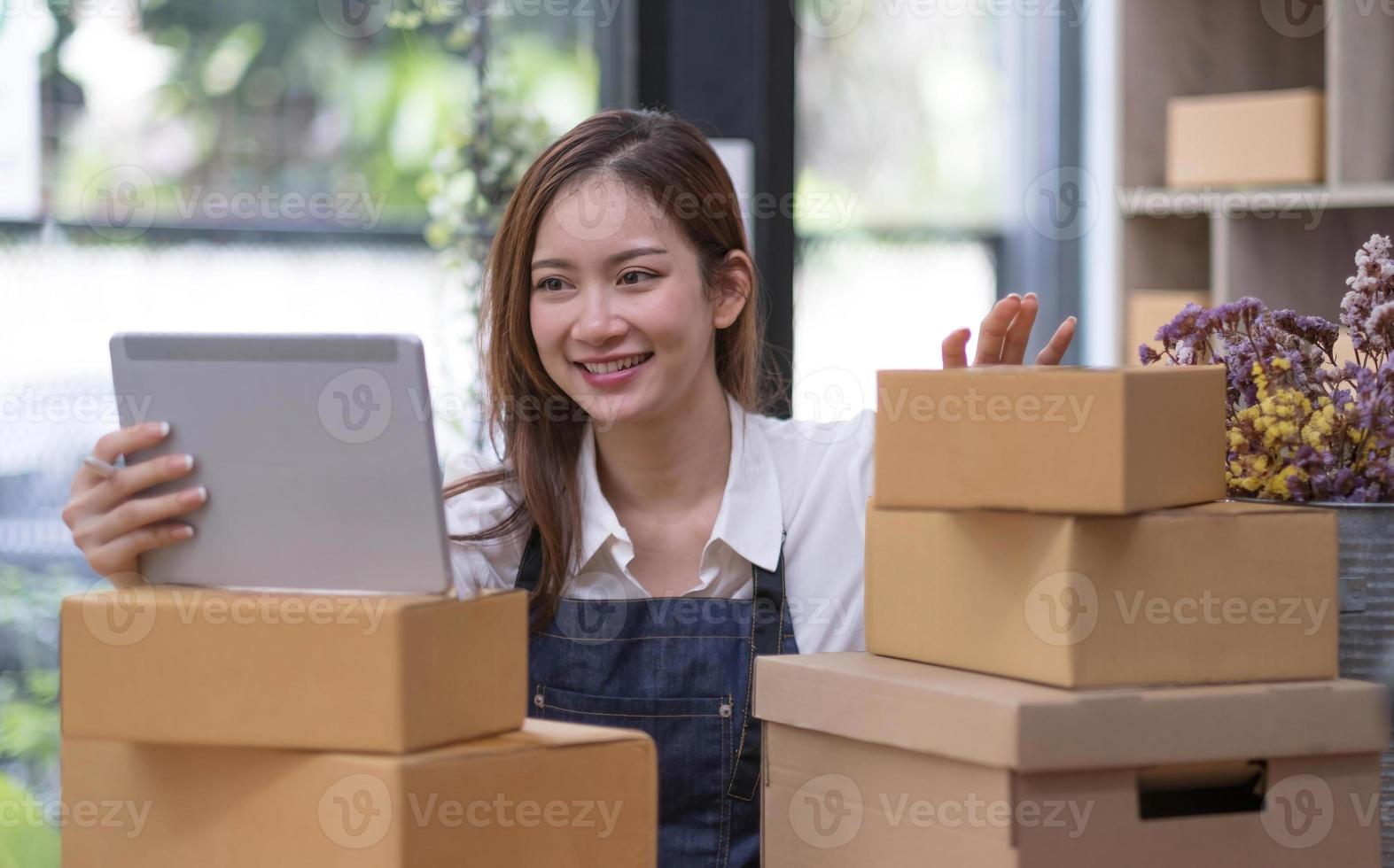 A portrait of a small startup, an SME owner, an Asian female entrepreneur checking orders to arrange the produce before packing the products in the inner boxes with the customers. Freelance concepts photo