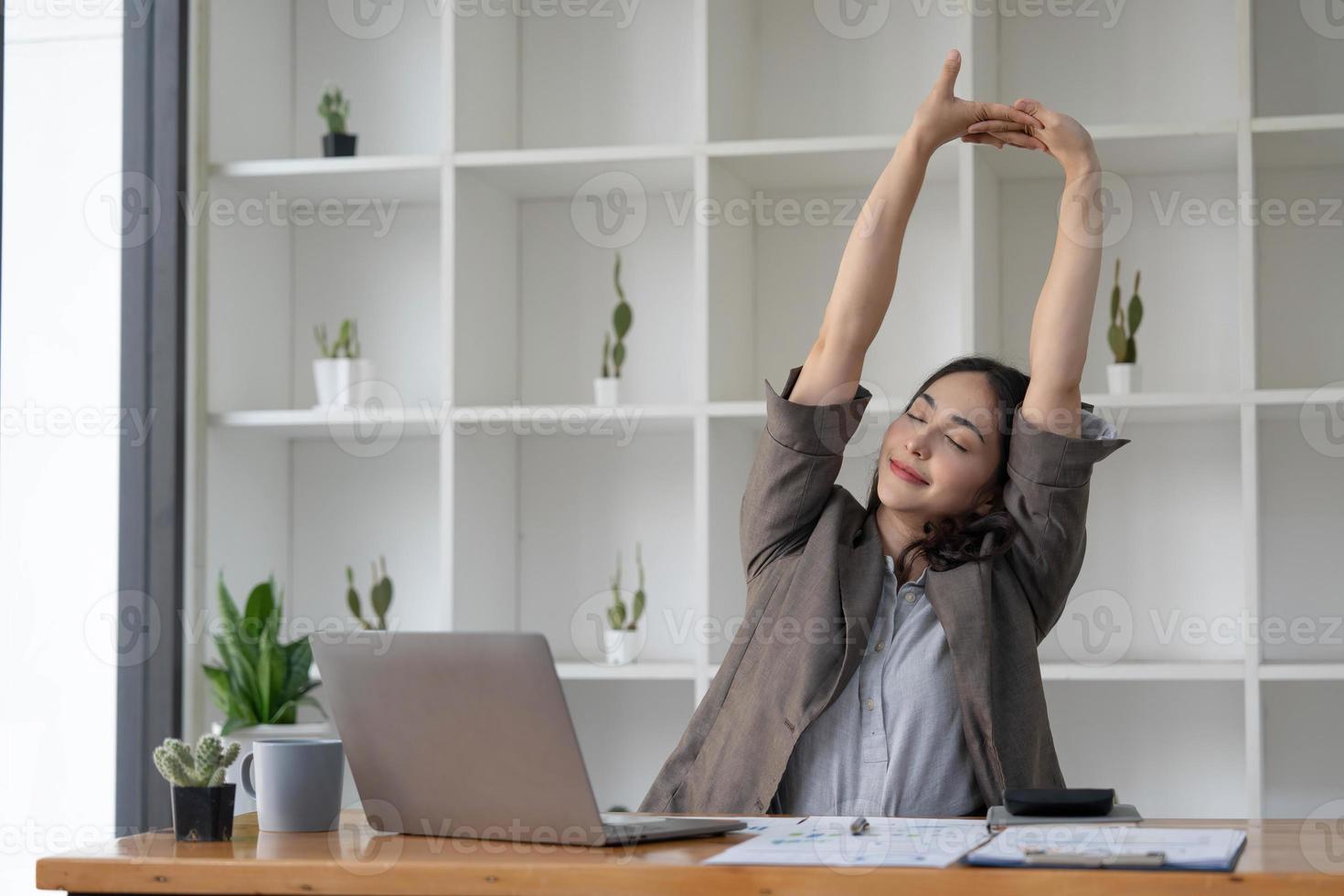 Asian businesswoman stretches her arms to relax her tired muscles from working at her desk all day at the office. photo