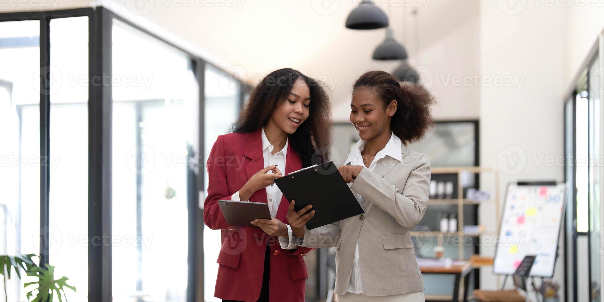 Smiling diverse colleagues businesswomen working on laptop together, looking at screen, stand at desk in office, employees discussing project strategy, sharing ideas photo