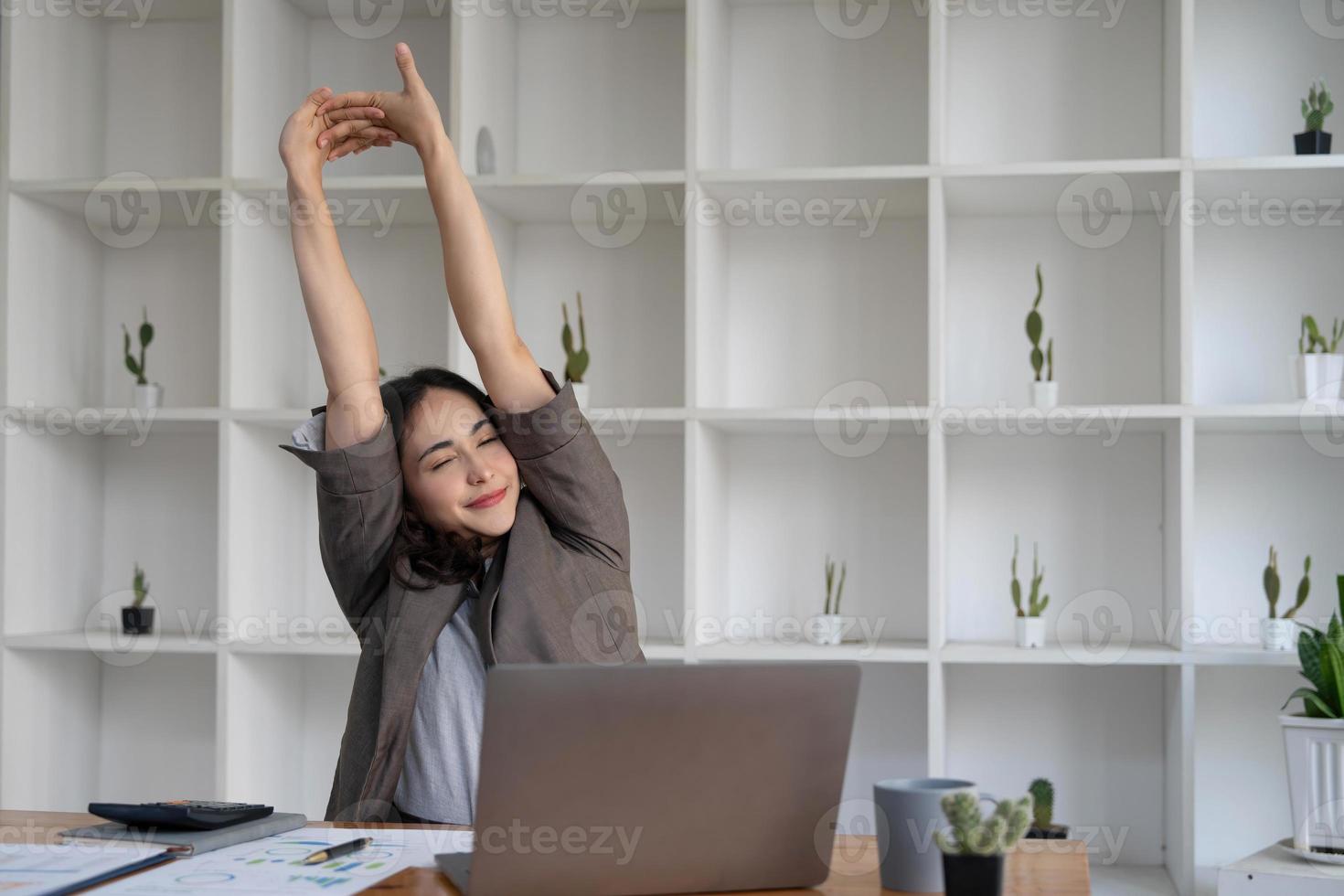 Asian businesswoman stretches her arms to relax her tired muscles from working at her desk all day at the office. photo