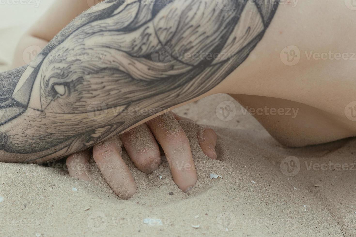 Cerrar joven mujer desnuda con tatuaje en la playa de arena concepto foto