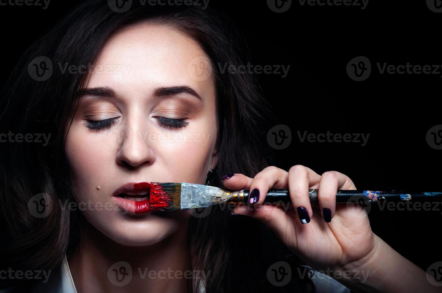 Makeup artist puts red lipstick . Beautiful female face. The hand of a makeup master, painting the lips of a young beautiful model. Makeup in the process photo