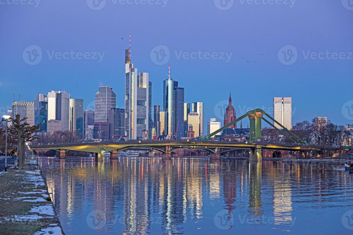 Picture of Frankfurt skyline during sunrise with reflections of skyscraper facades in Main river under cloudless and colorful sky photo
