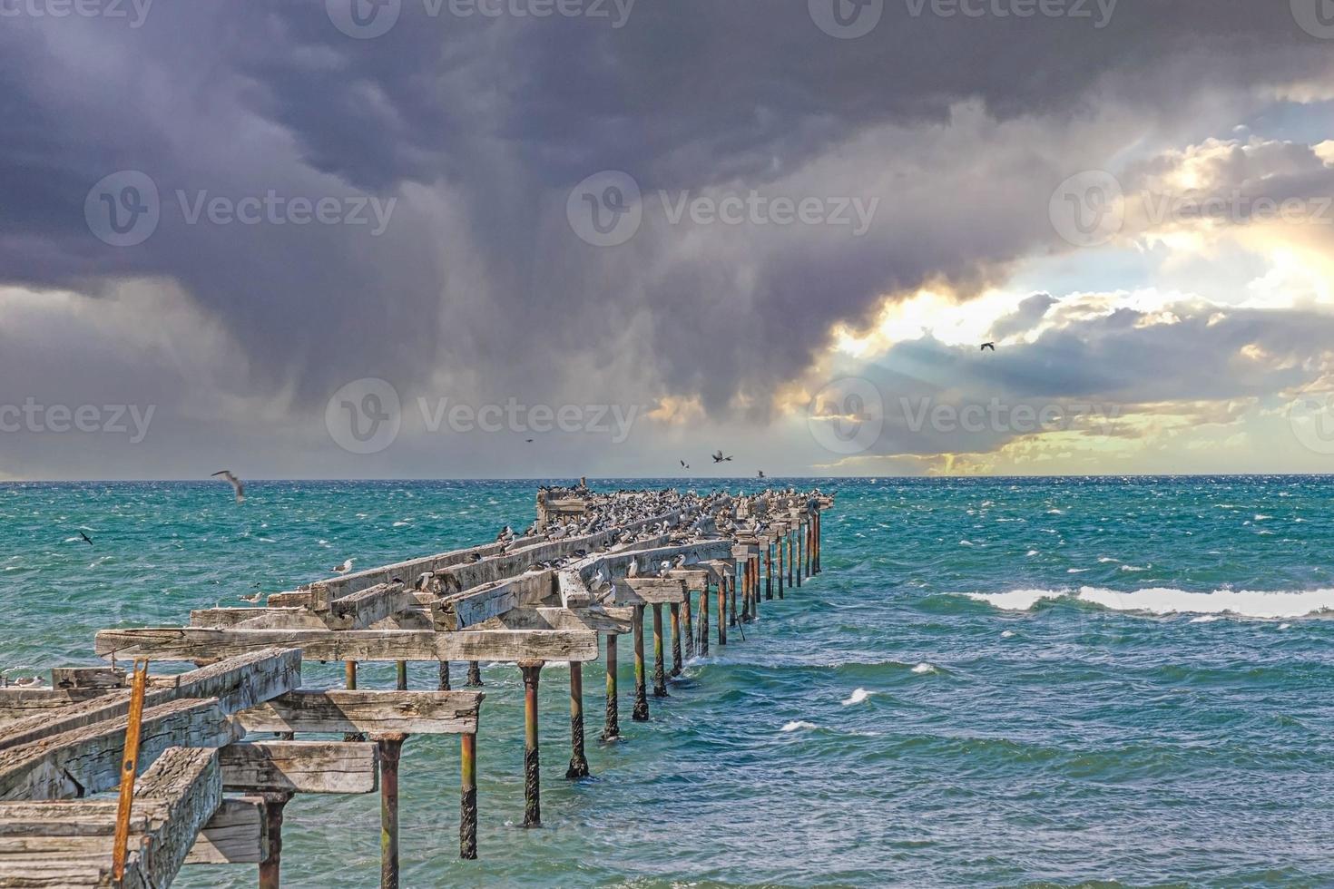 Image of dilapidated jetty with seagulls resting on it against a sky with storm clouds photo