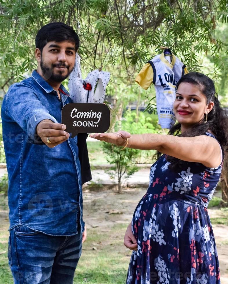 Indian couple posing for maternity baby shoot. The couple is posing in a lawn with green grass and the woman is falunting her baby bump in Lodhi Garden in New Delhi, India photo