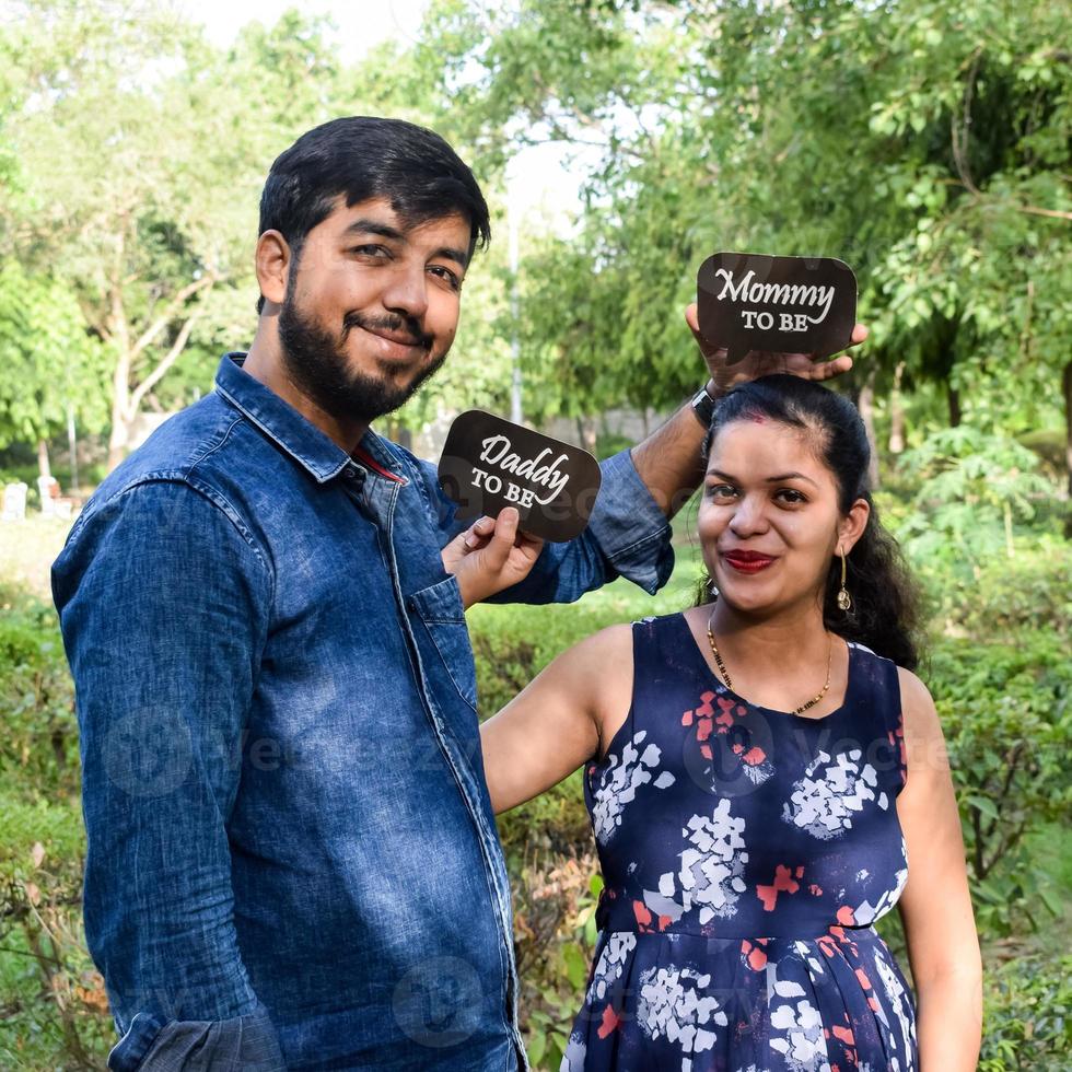 Indian couple posing for maternity baby shoot. The couple is posing in a lawn with green grass and the woman is falunting her baby bump in Lodhi Garden in New Delhi, India photo