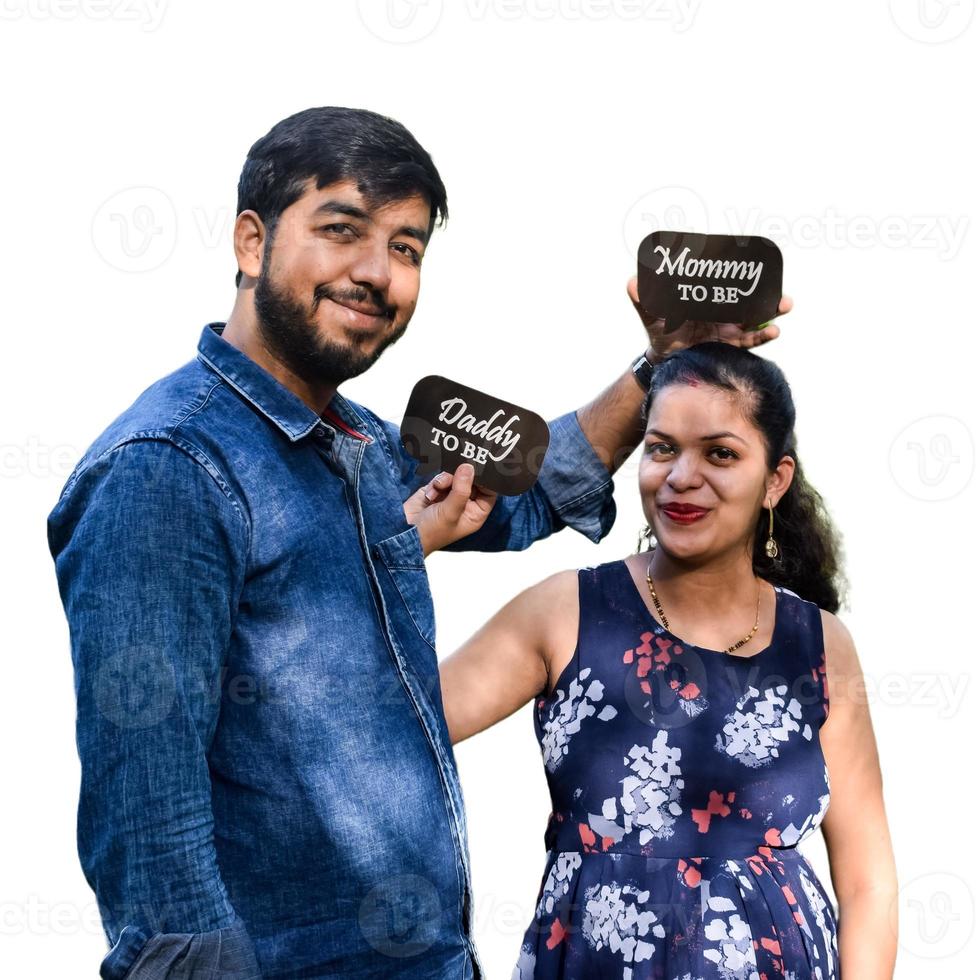 Indian couple posing for maternity baby shoot with white plain background. The couple is posing in a lawn with green grass and the woman is falunting her baby bump in Lodhi Garden in New Delhi, India photo