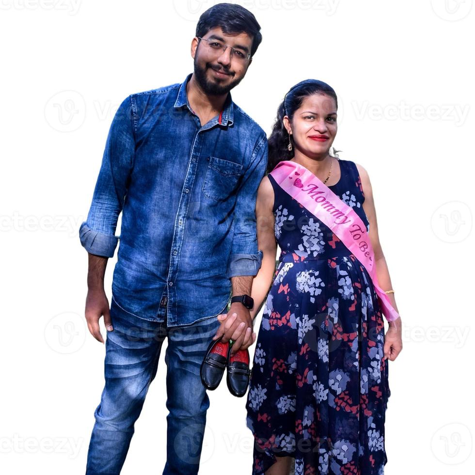 Indian couple posing for maternity baby shoot with white plain background. The couple is posing in a lawn with green grass and the woman is falunting her baby bump in Lodhi Garden in New Delhi, India photo