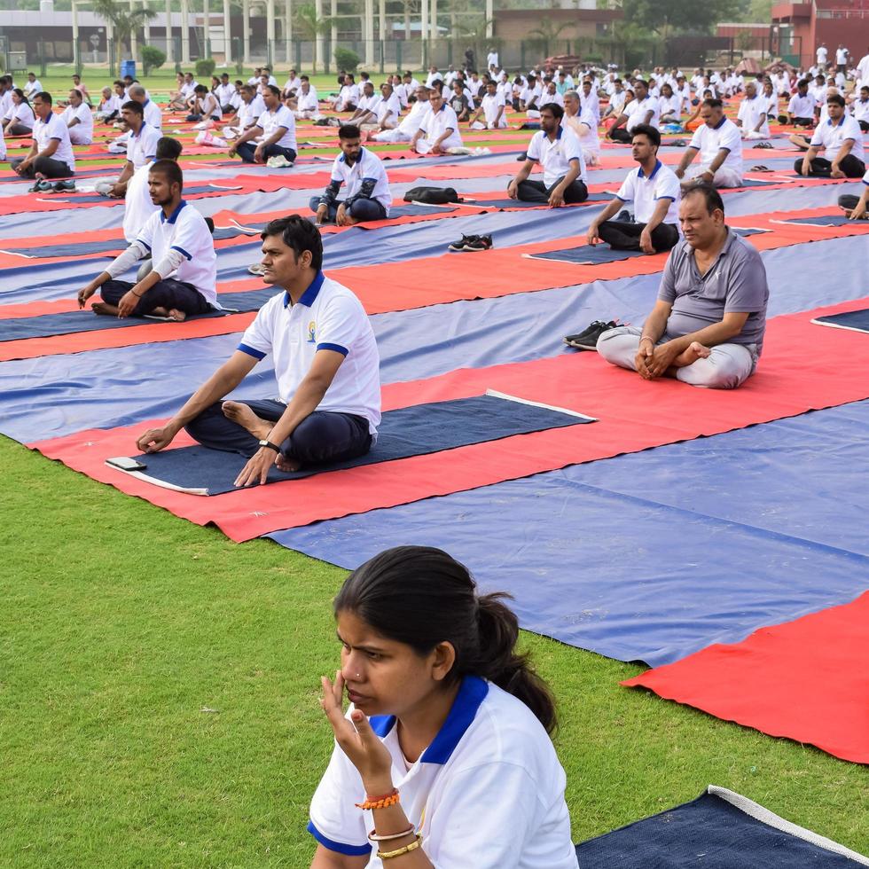 New Delhi, India, June 21 2022 - Group Yoga exercise session for people at Yamuna Sports Complex in Delhi on International Yoga Day, Big group of adults attending yoga class in cricket stadium photo