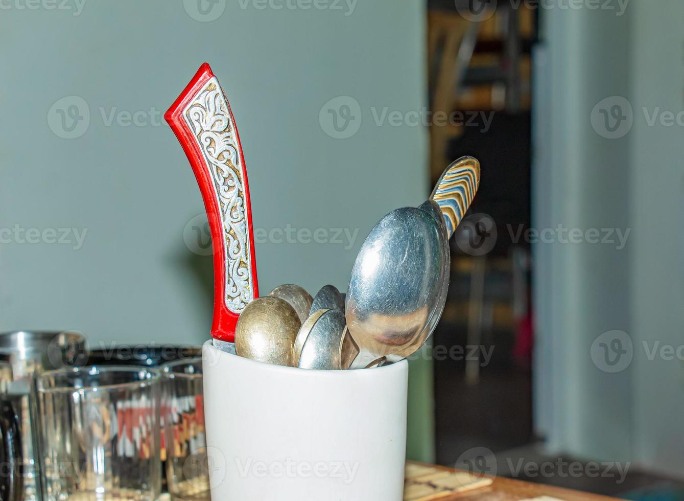 recipiente blanco lleno de cucharas, tenedores y cuchillos sobre una mesa en una cocina con un fondo borroso foto