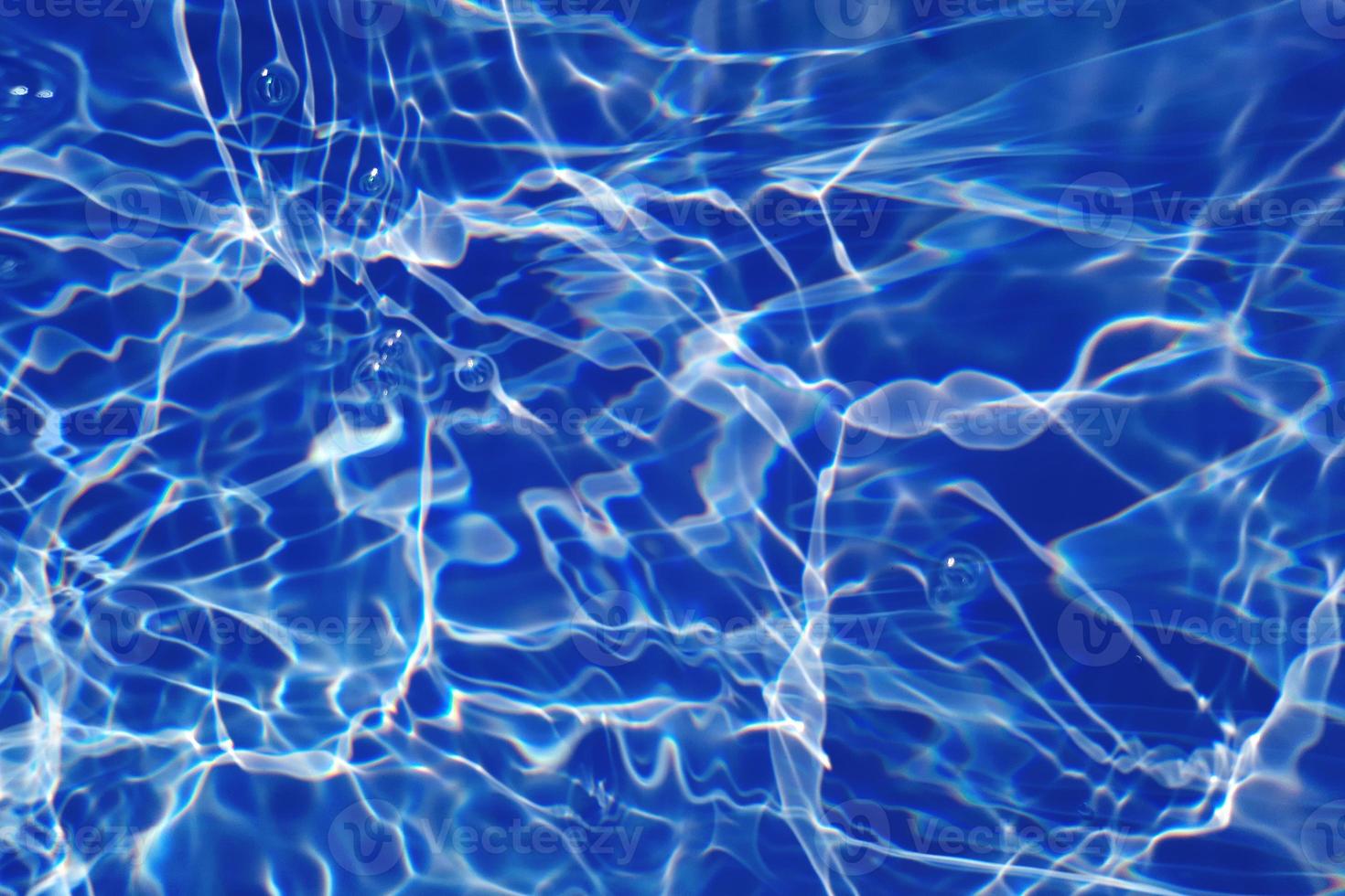 Defocus blurred transparent blue colored clear calm water surface texture with splashes and bubbles. Trendy abstract nature background. Water waves in sunlight with caustics. Blue water shinning photo