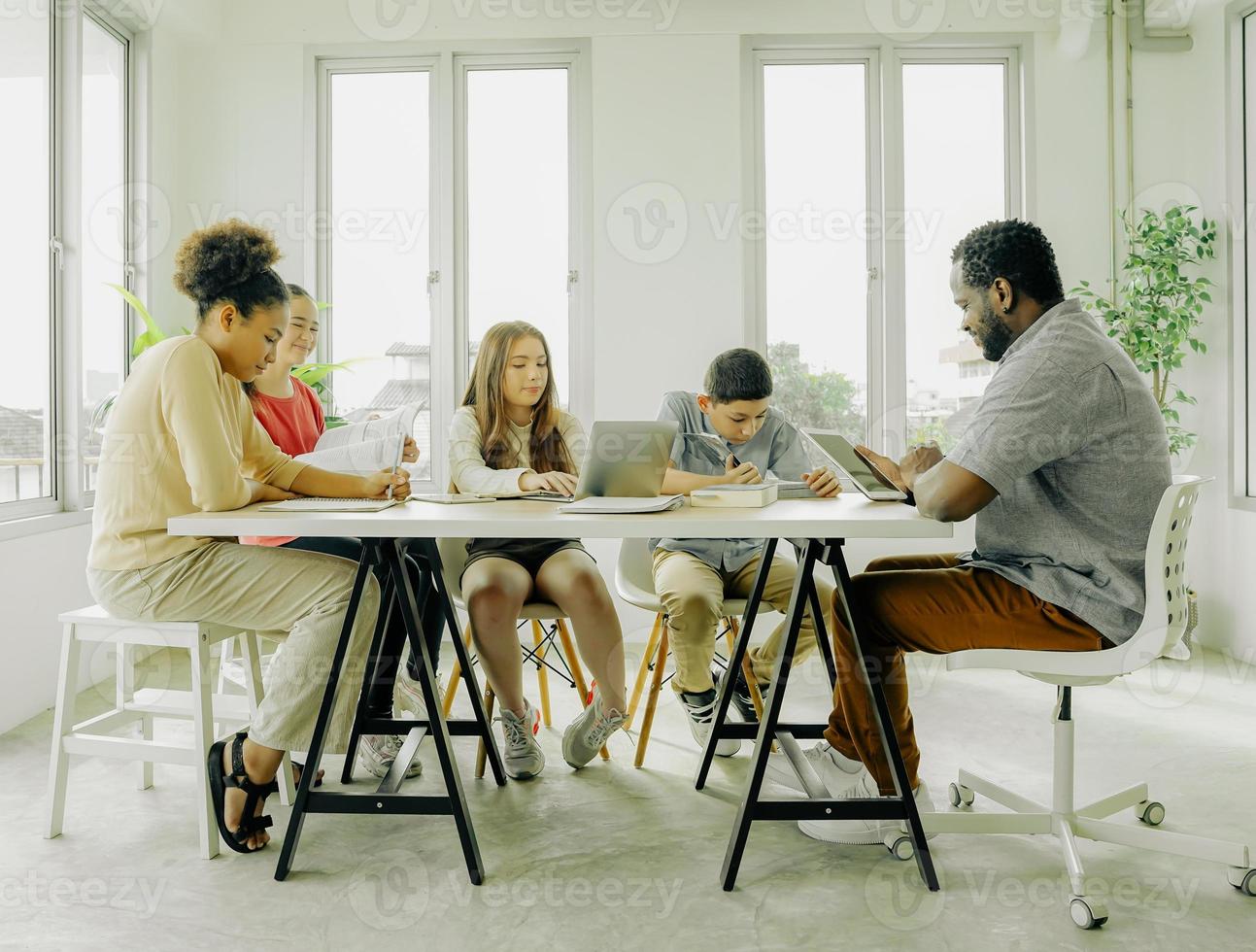Group of diverse children sitting in classroom learning, reading book and asking teacher at school. Teenage student and classmate back to school together studying lessons. Diversity friendship concept photo