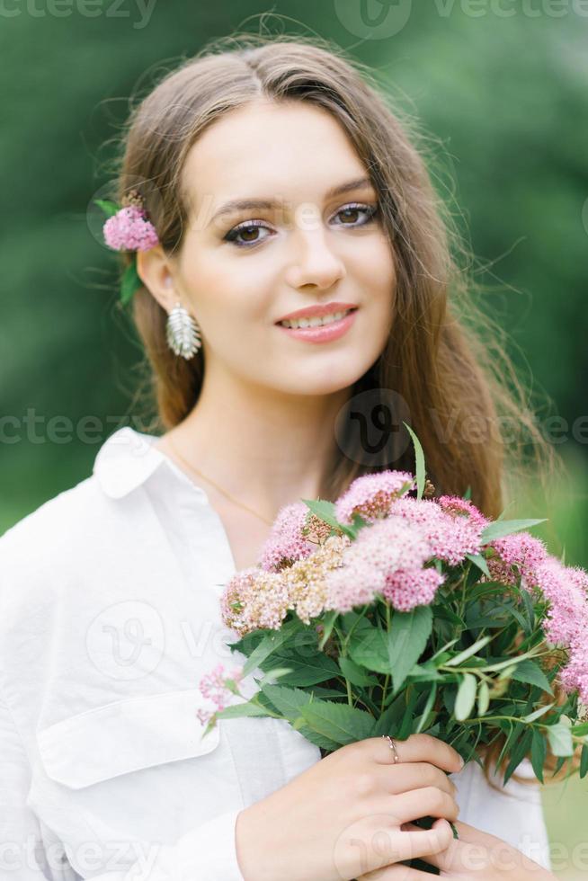 Outdoor close-up portrait of a beautiful young woman with pink flowers on a sunny day in the park. A happy woman received a bouquet of garden flowers from her boyfriend as a gift photo