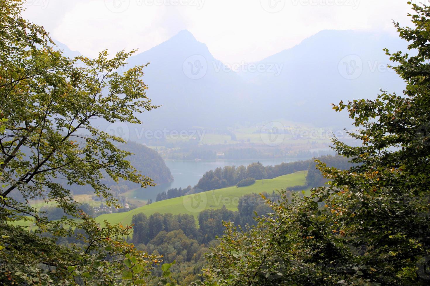 viaje a sankt-wolfgang, austria. la vista sobre un bosque y un prado con un lago y las montañas al fondo. foto
