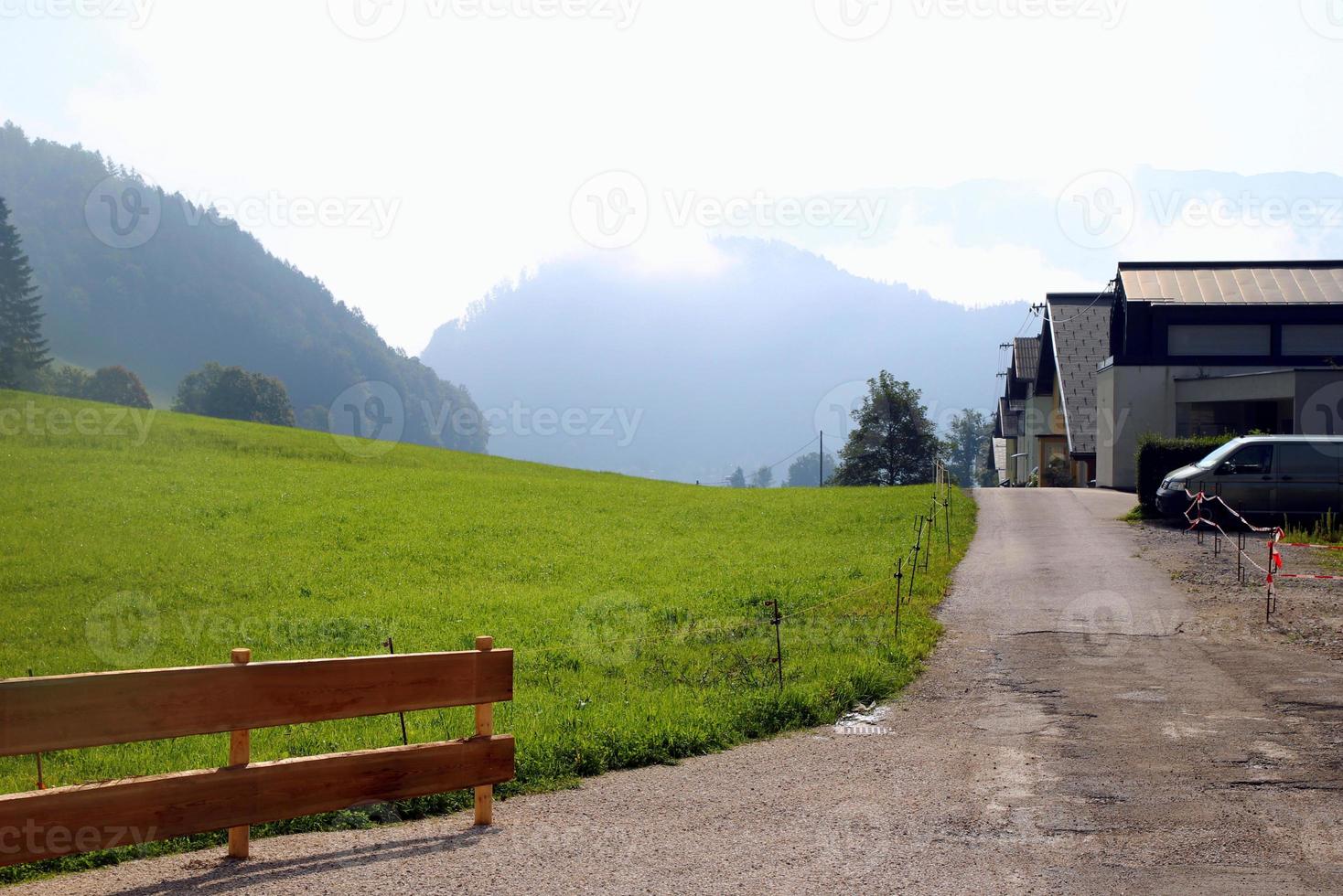 viaje a sankt-wolfgang, austria. la vista de la carretera cerca del prado verde con las casas y las montañas al fondo. foto