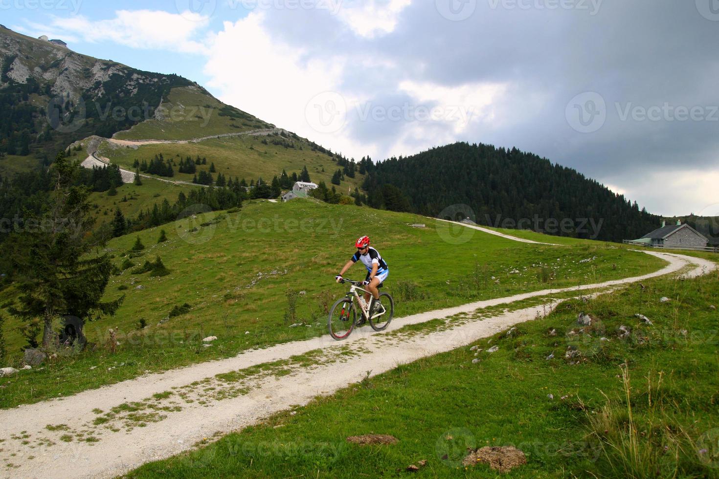 Travel to Sankt-Wolfgang, Austria. A cyclist on the road between the fields with view on the mountains and the houses in the clouds. photo