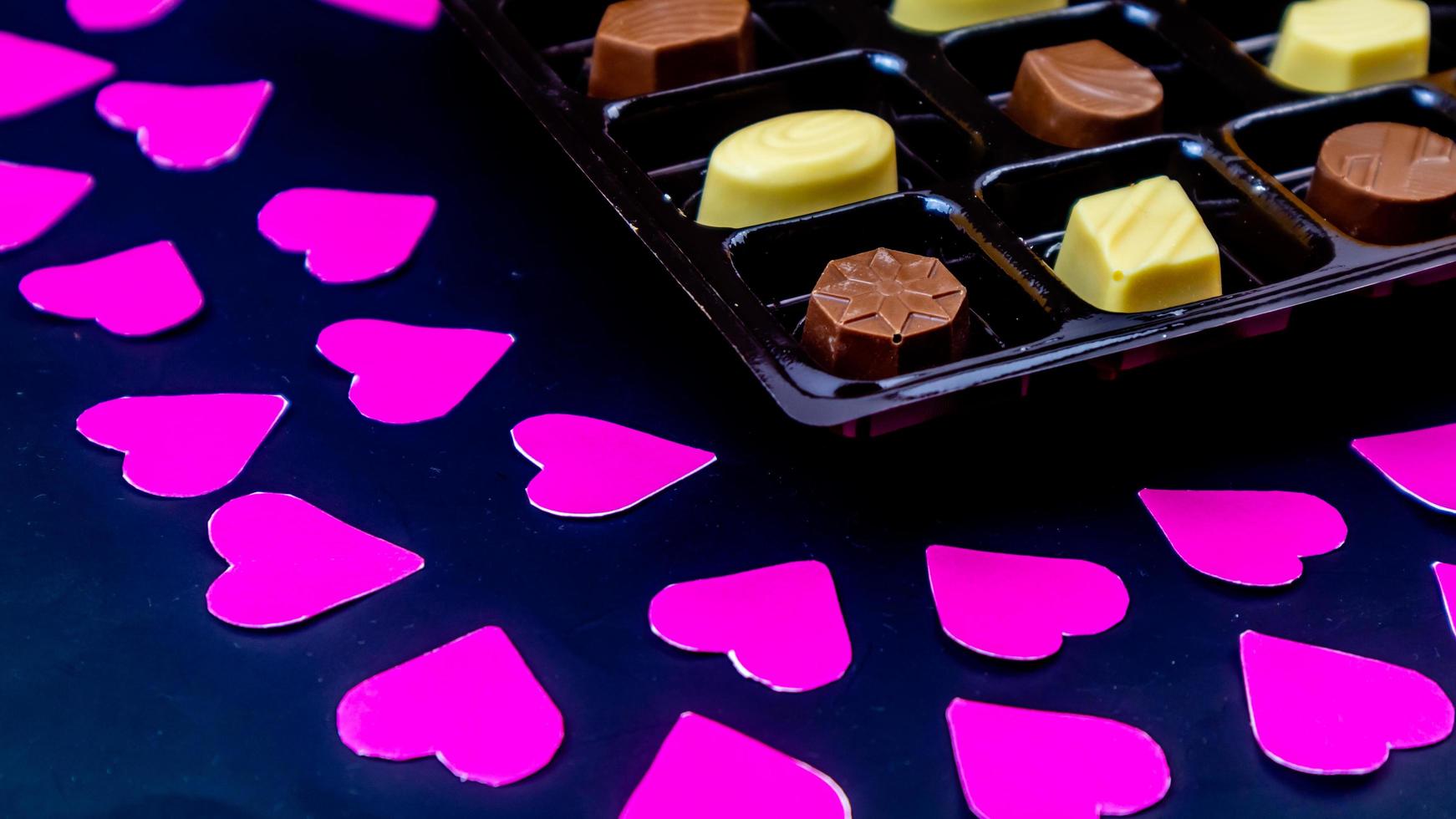 delicioso chocolate rodeado de corazones rosas sobre fondo negro foto