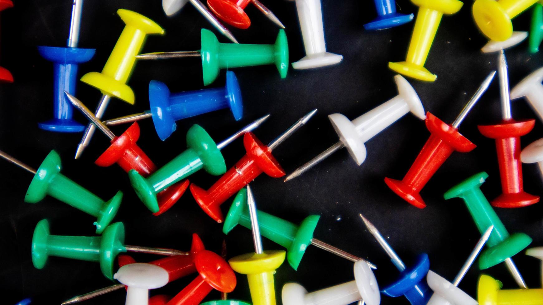 multicolored thumbtacks on a black background photo