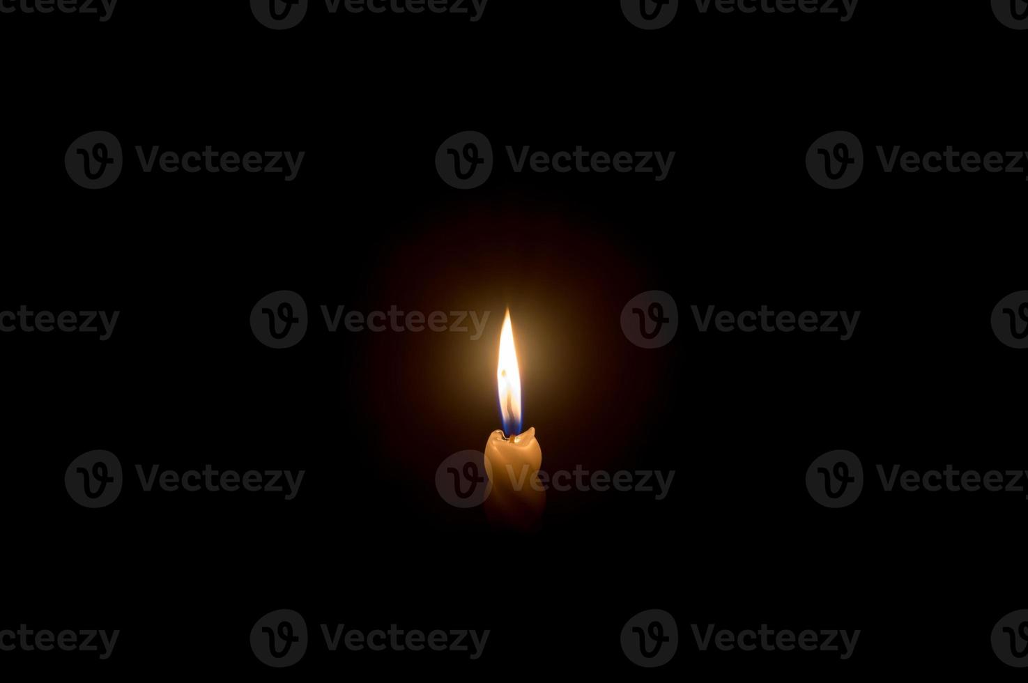 A single burning candle flame or light glowing on a spiral white candle on black or dark background on table in church for Christmas, funeral or memorial service photo