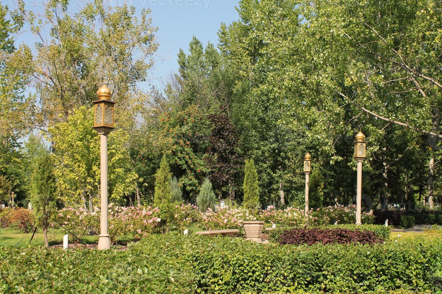 Trees and flowers in city park with Indian style lantern. Pedestrian zone for walking. Urban planning, public space concept. Town recreation area. Architecture design comfortable garden. Footpath way photo