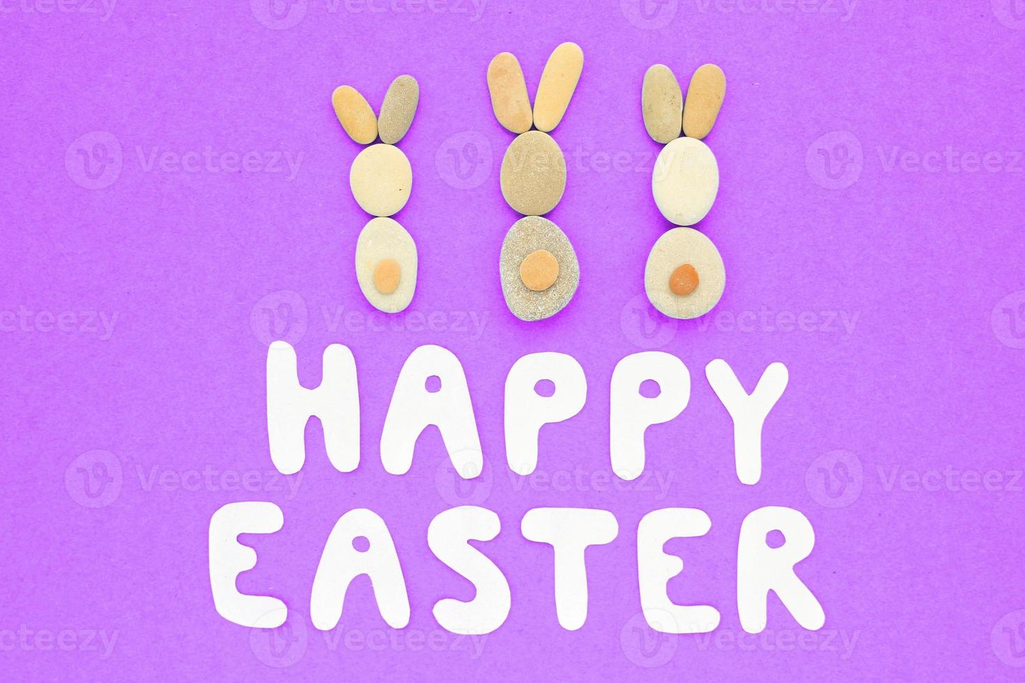 Happy Easter lettering and bunnies from pebbles on violet background. Flatlay postcard creative concept. Creative greetings with natural craft ecological materials. Save the planet, zero waste idea. photo